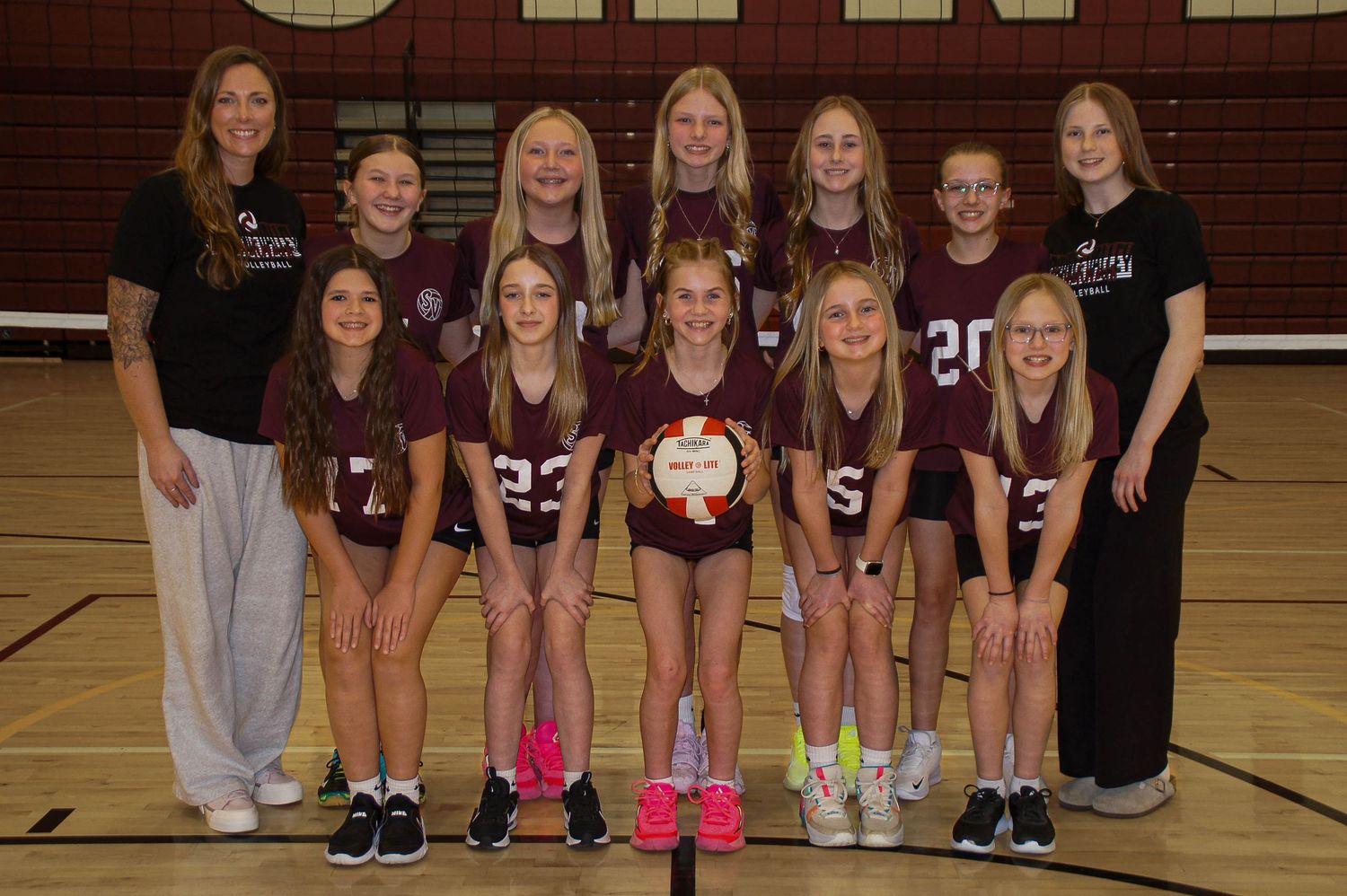 Spring Valley youth volleyball team poses for a group photo inside a gymnasium with their coach.