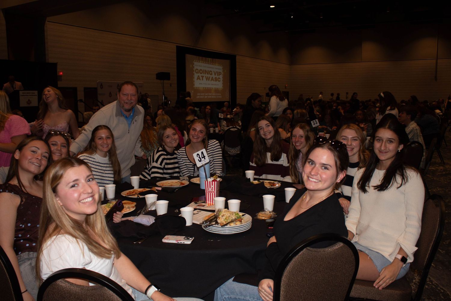 A group of smiling students gather around a table at a leadership conference dinner.