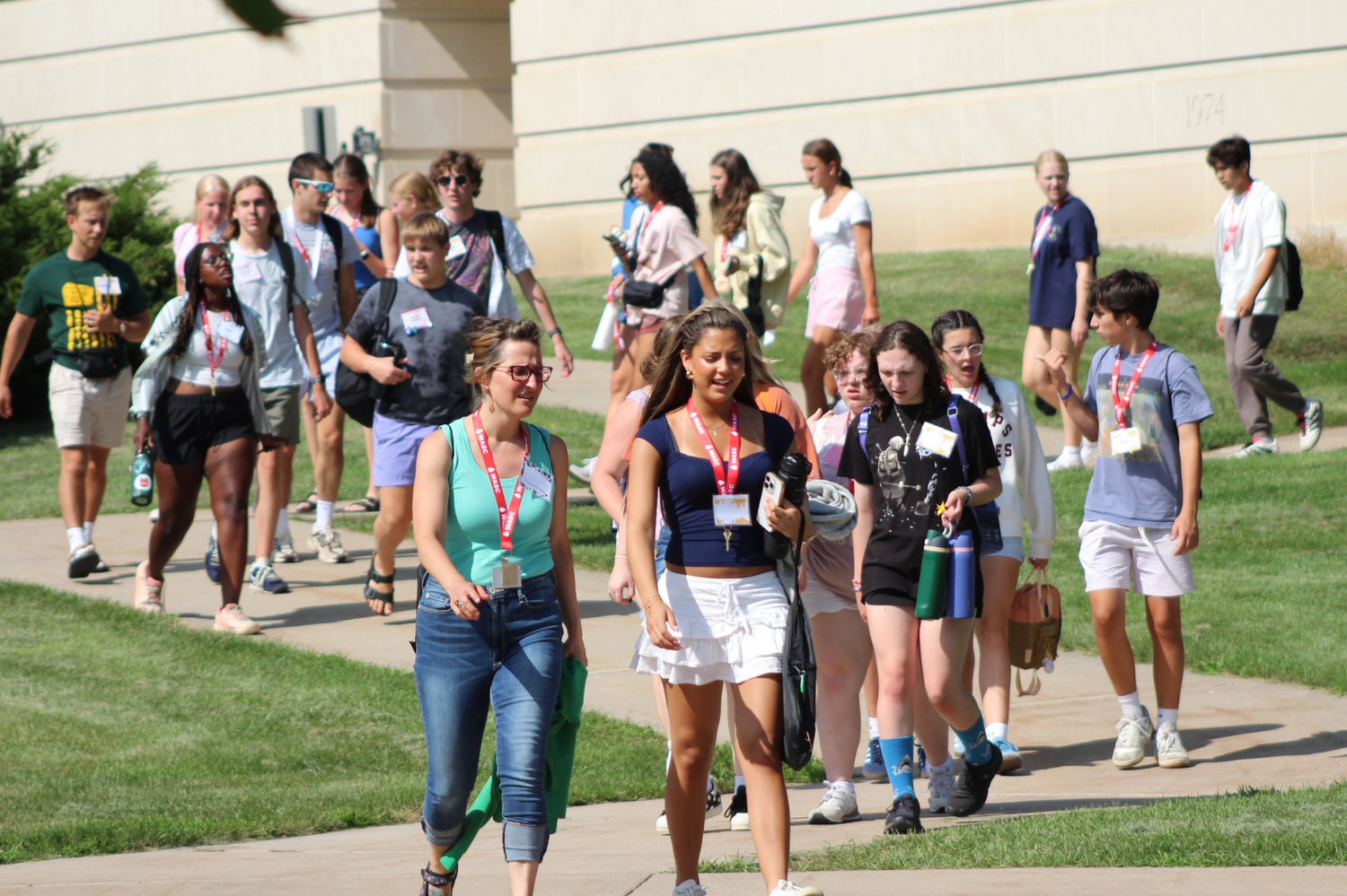 Group of college students and staff walk together along a sunny campus sidewalk during an orientation tour.