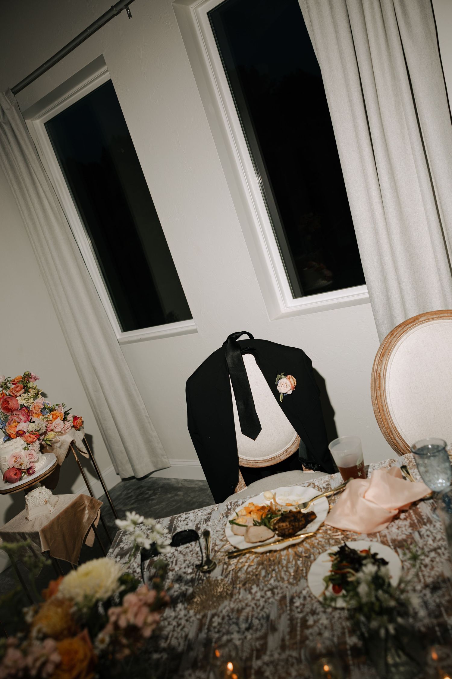 Groom's black suit jacket with boutonniere draped over chair at floral-decorated wedding sweetheart table.