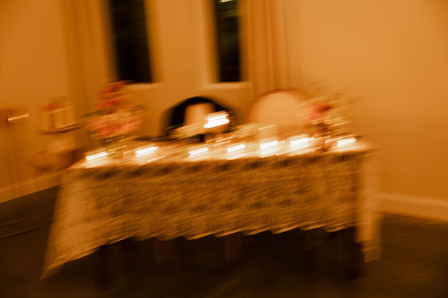Softly blurred warm-toned photo of a decorated wedding sweetheart table with candles and floral arrangements.