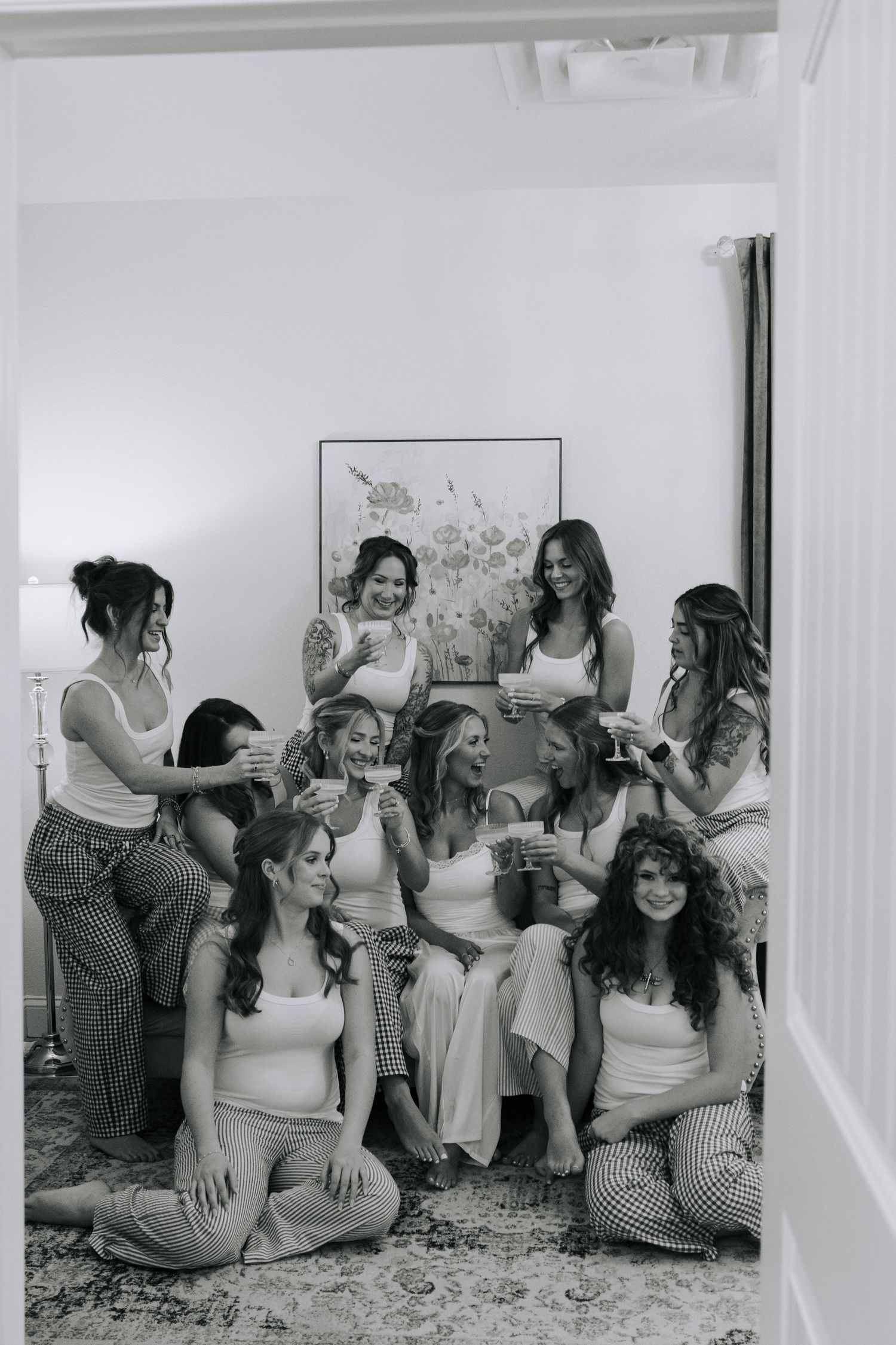 Black and white photo of bridesmaids laughing and celebrating together in a cozy room during bridal party preparations.