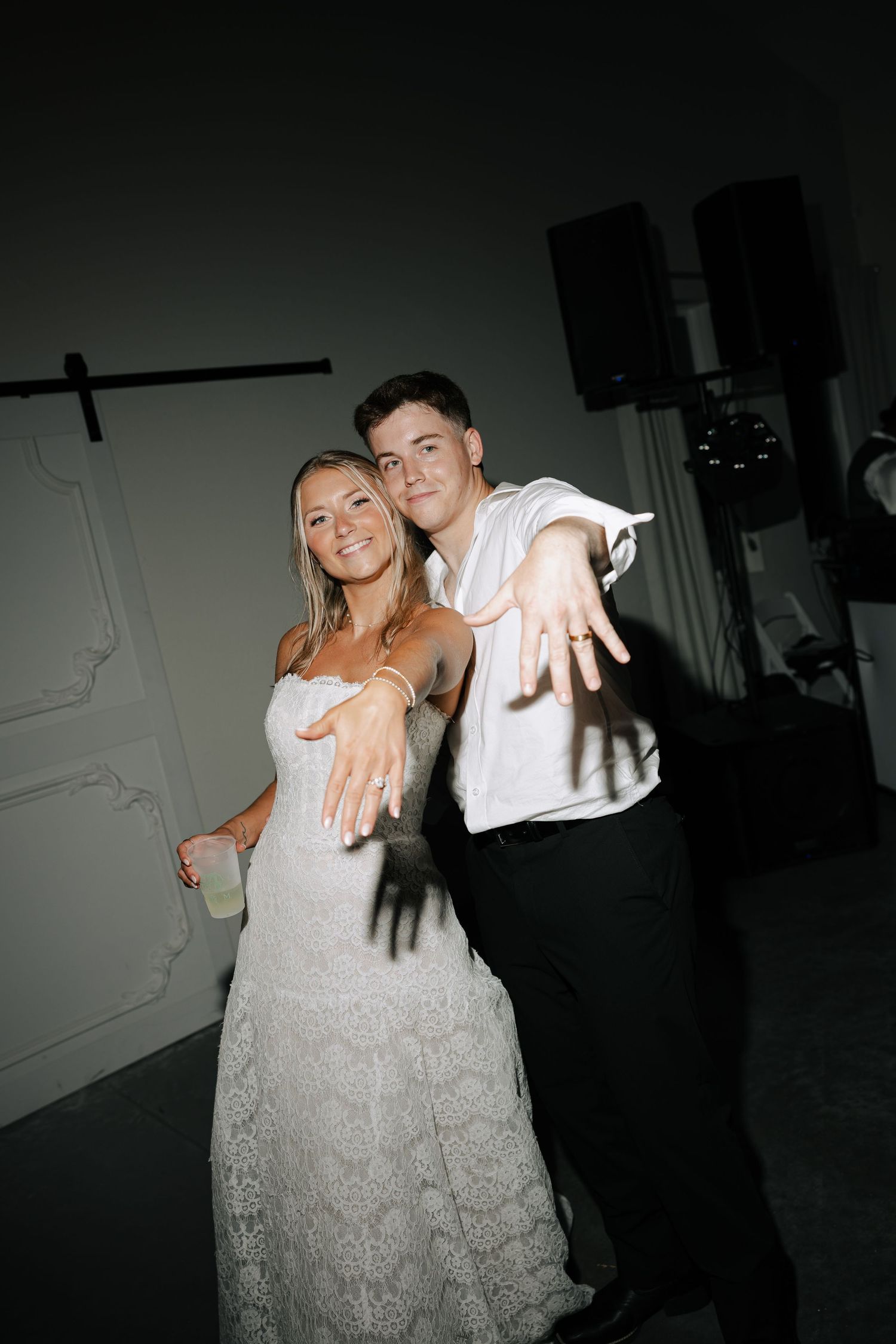 Joyful newlyweds showing off their wedding rings to the camera on the dance floor at their reception.