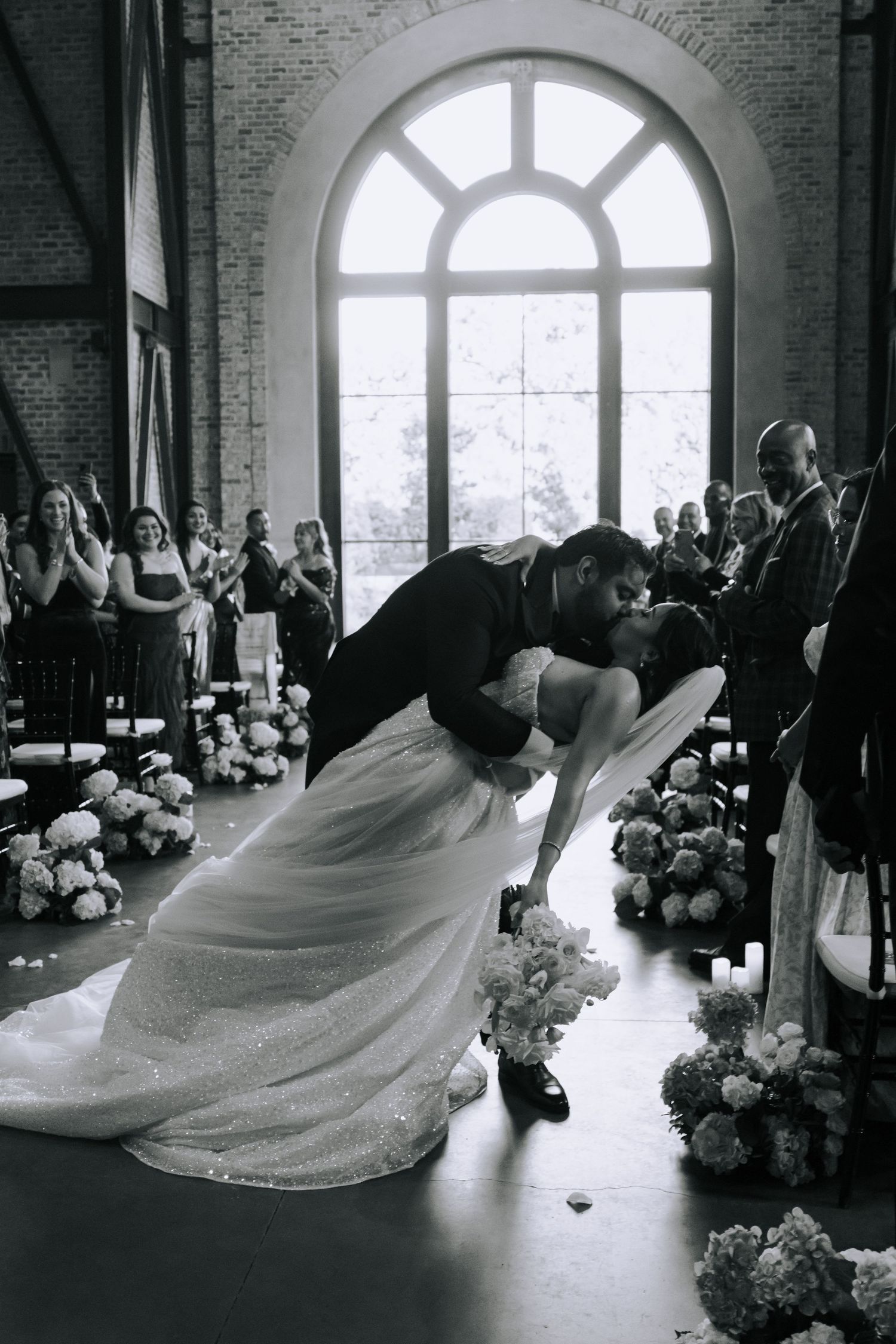 Black and white photo of bride and groom sharing a romantic dip kiss at the altar during their wedding ceremony.