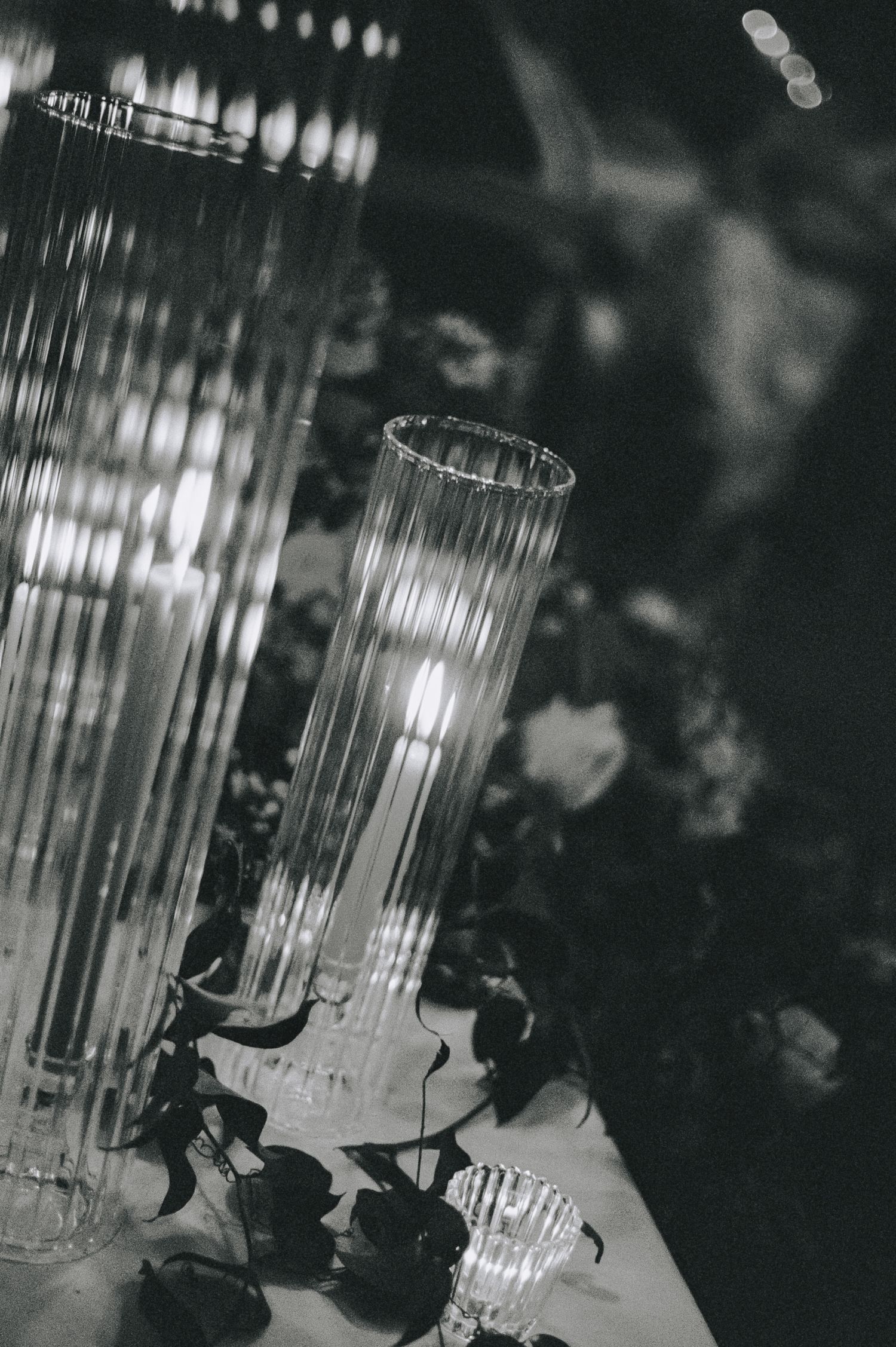 Black and white close-up of tall ribbed glass candle holders on a floral decorated wedding table.