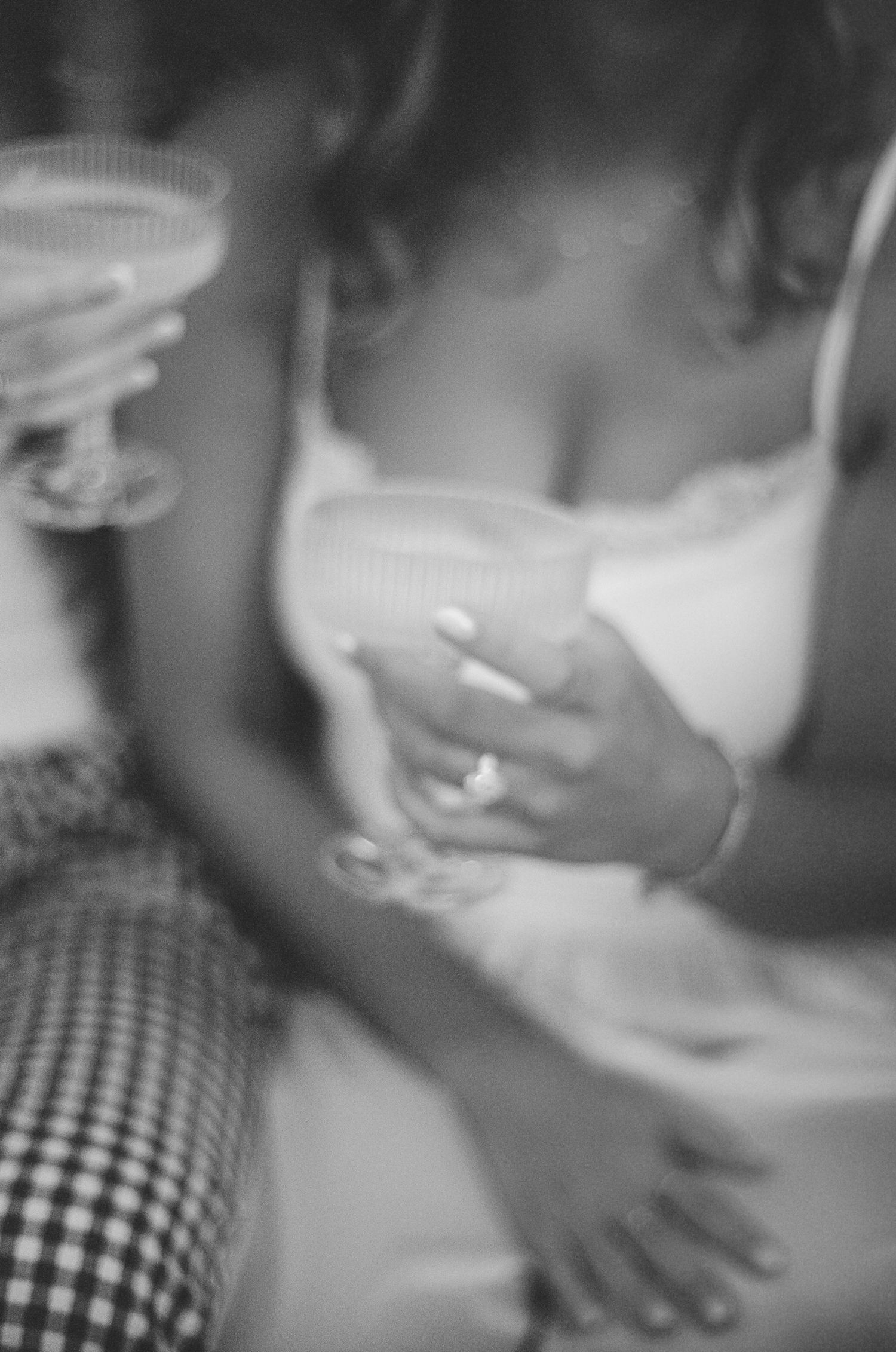 Black and white photo of a woman in a white camisole holding a cocktail glass, wearing a ring, with checkered pants.