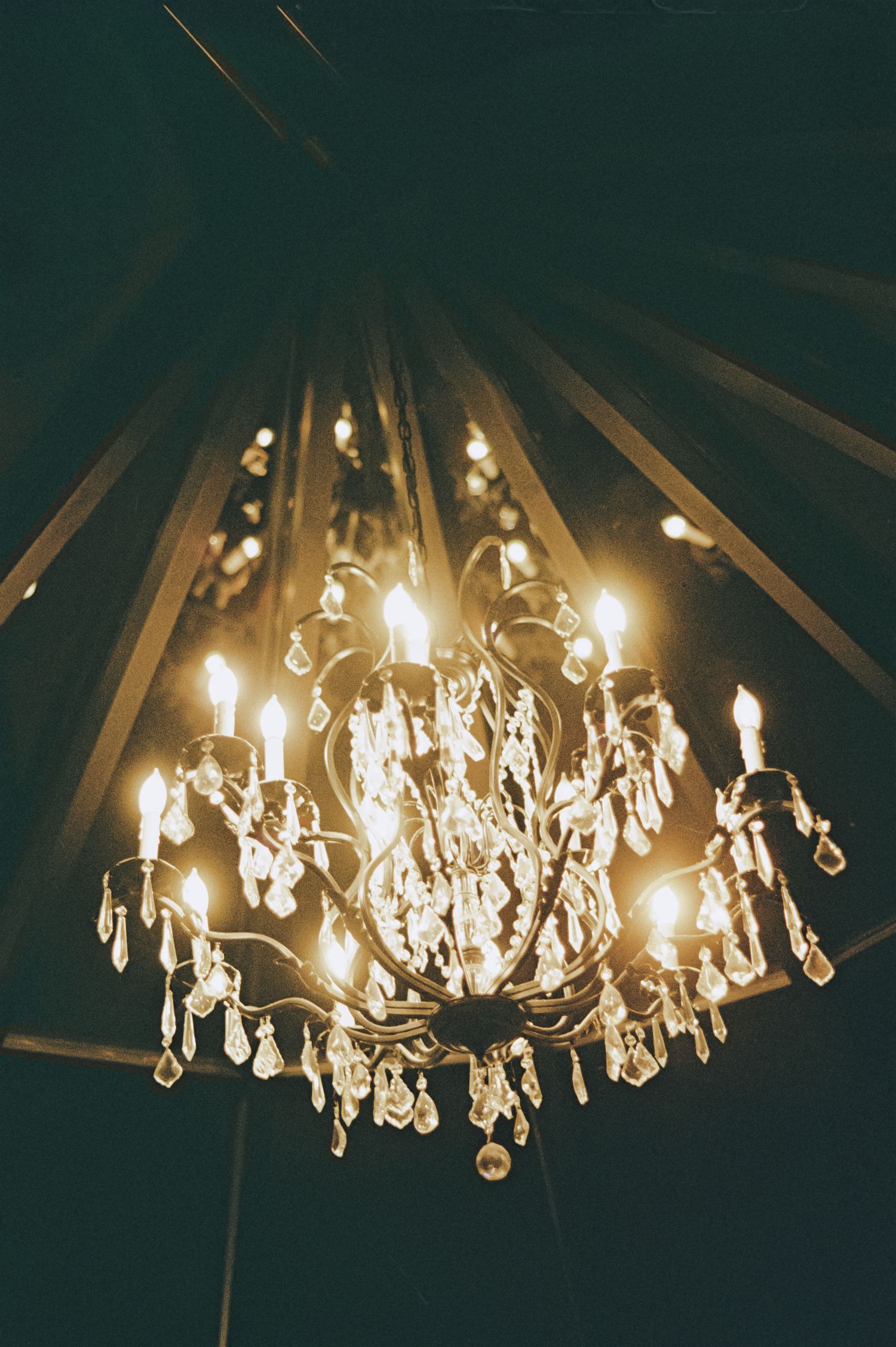 Elegant crystal chandelier glowing warmly against dark draped ceiling at a romantic wedding venue.