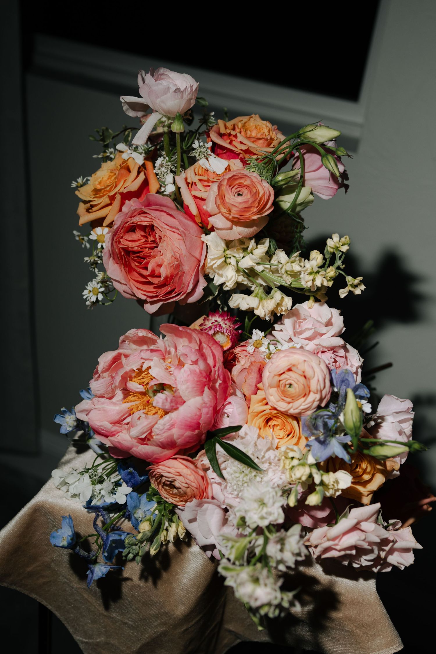 Lush bridal bouquet featuring pink peonies, peach roses, and blue wildflowers.
