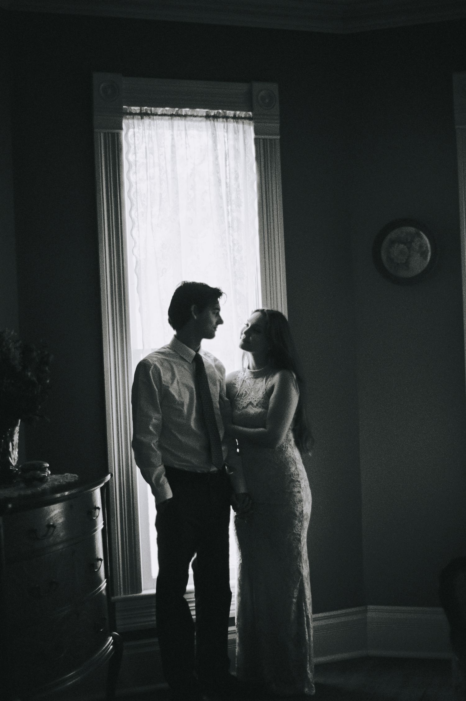 Black and white silhouette of a couple standing together by a tall window in a vintage-style room.