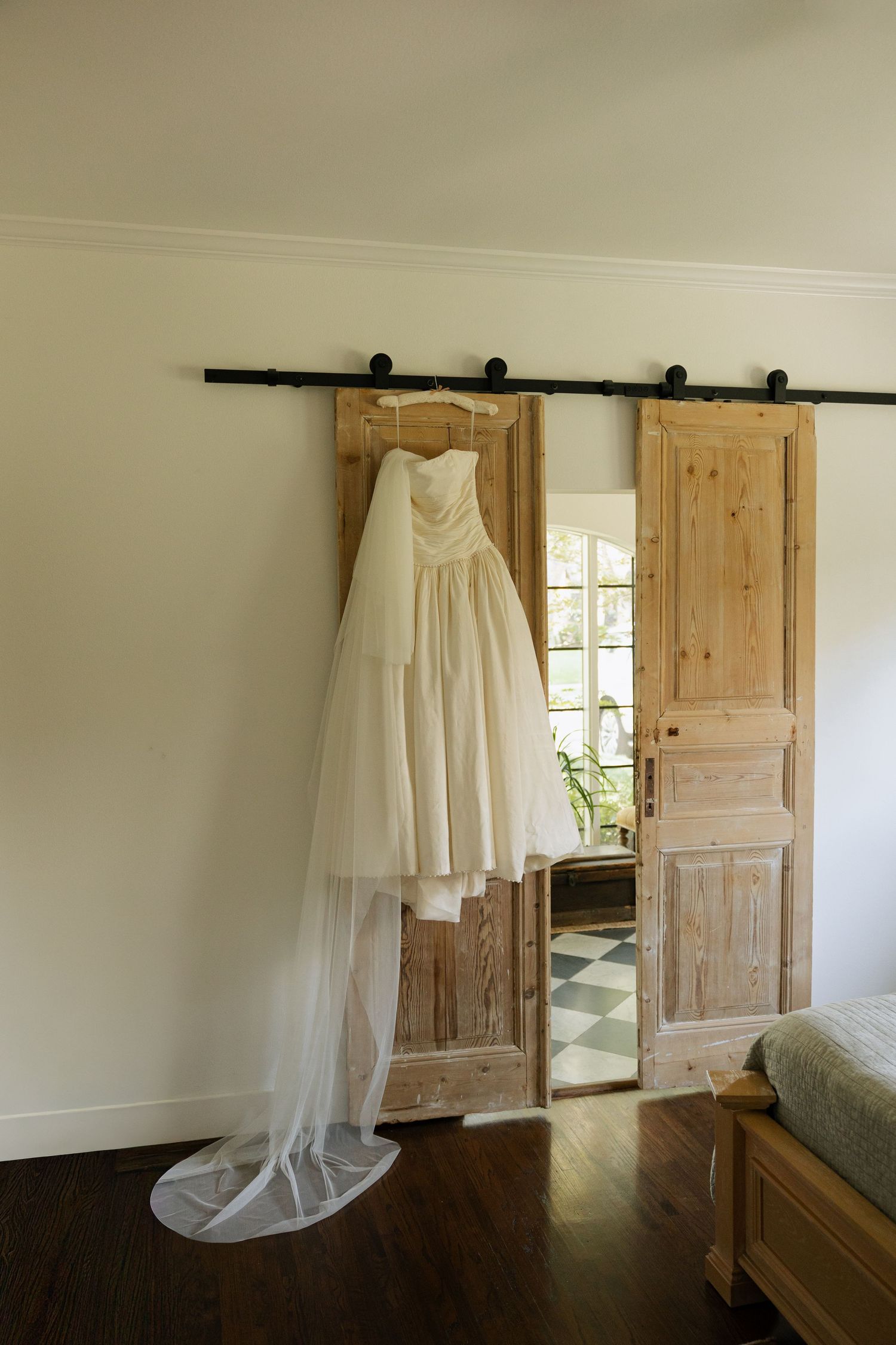 White wedding dress with veil hanging on rustic wooden barn sliding doors in a bright bedroom.