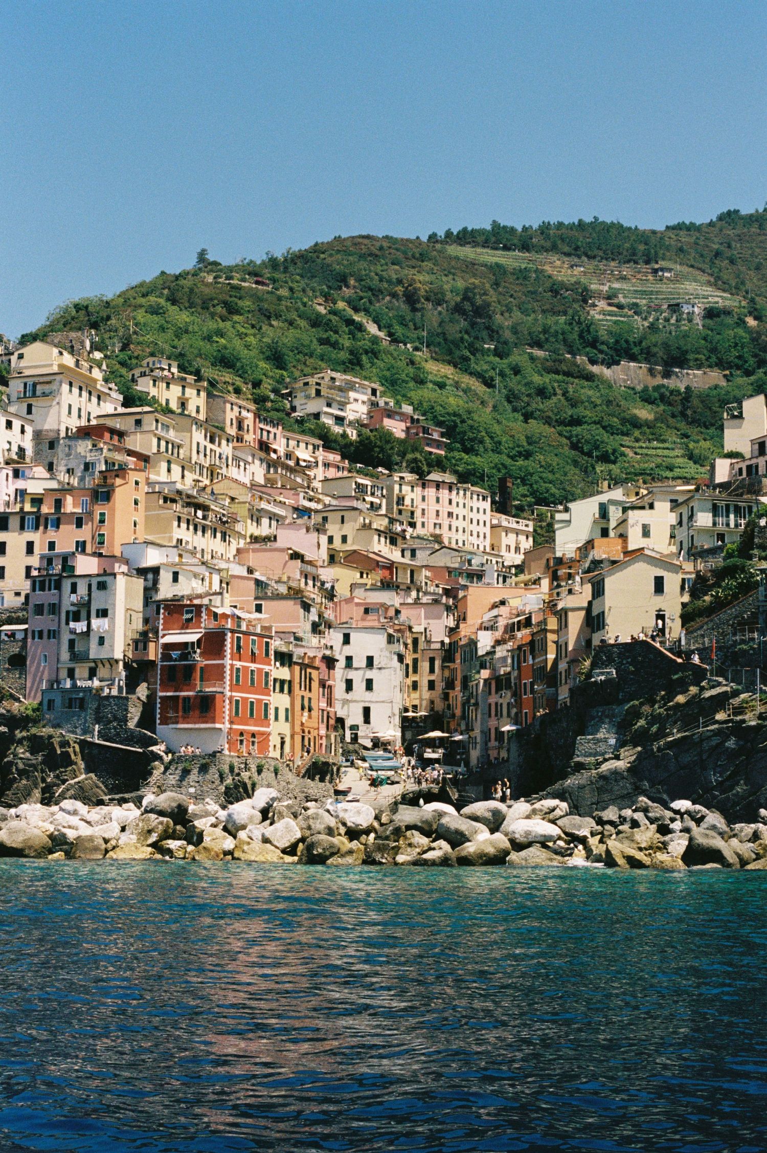 Colorful buildings cascade down a rocky hillside to the sea in Riomaggiore, one of Italy's scenic Cinque Terre villages.