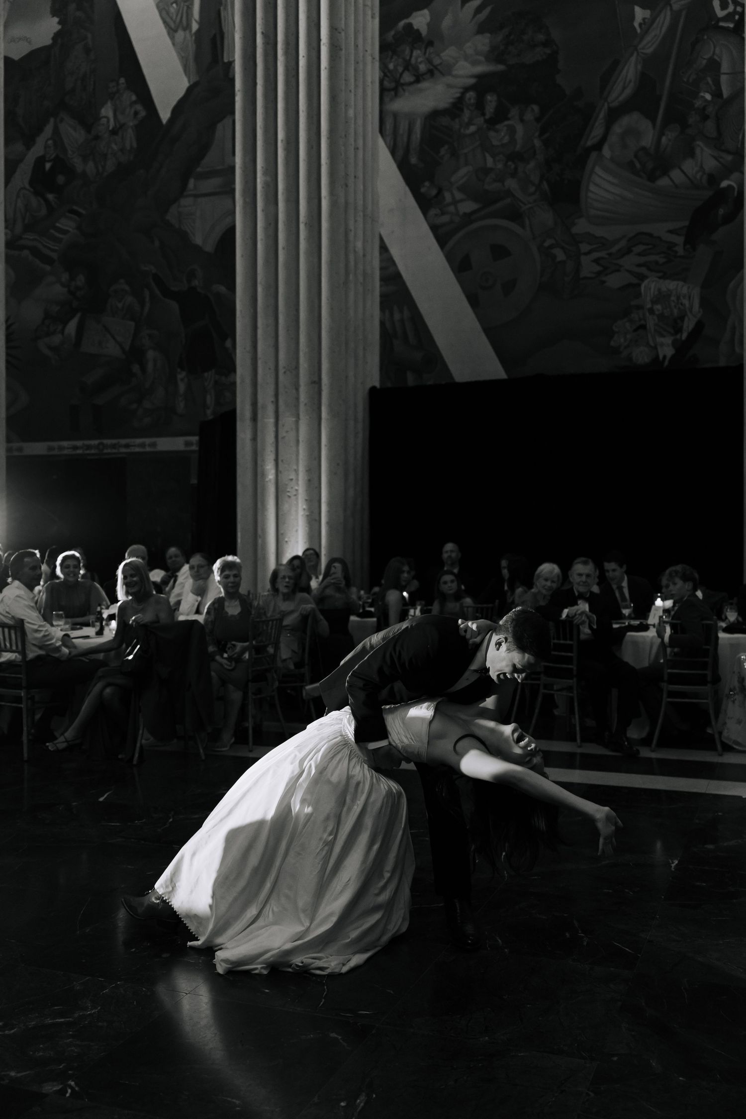 Black and white photo of a couple sharing a romantic dip dance at an elegant wedding reception.