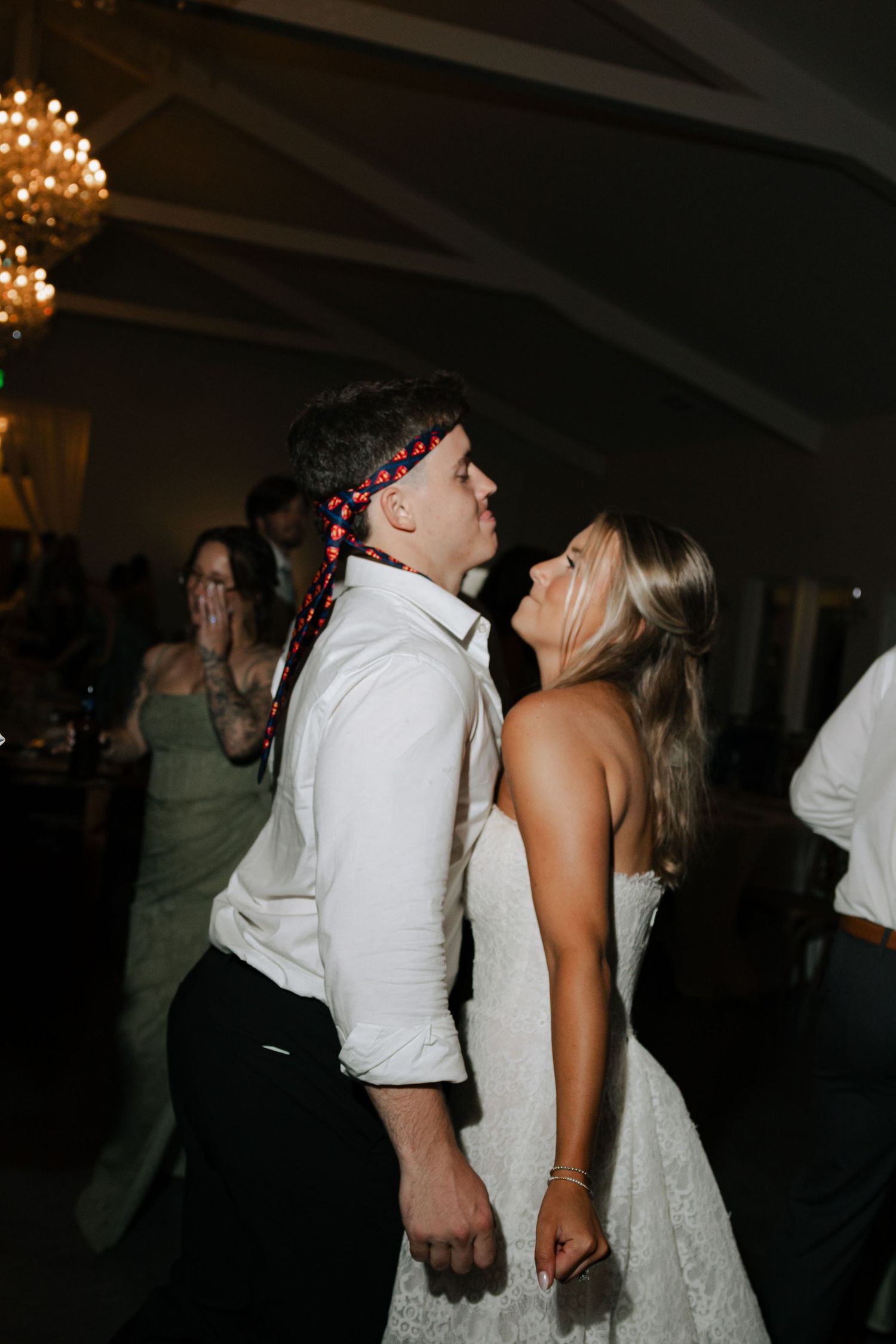 Bride and groom share a romantic dance together at their wedding reception under warm chandelier lighting.