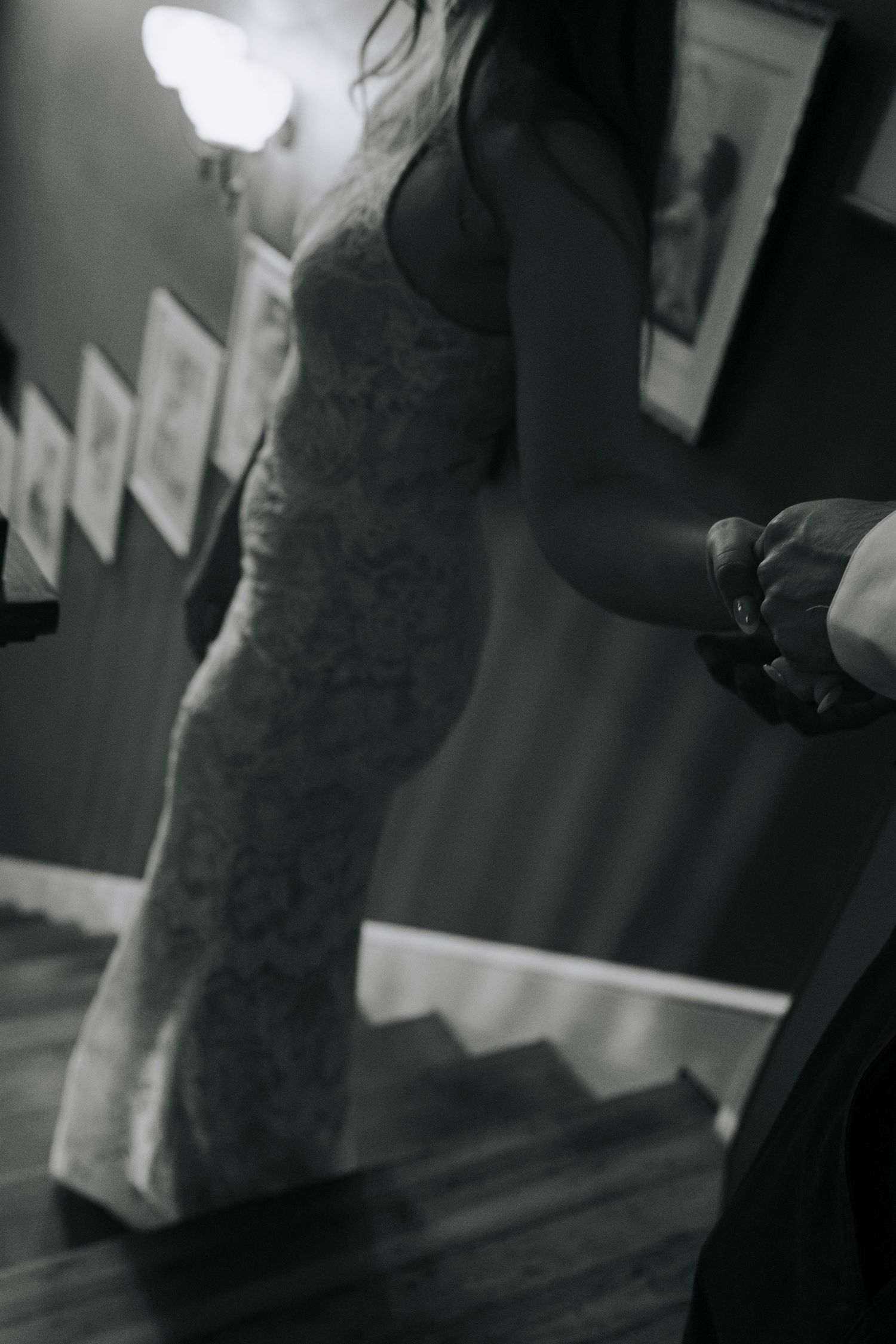 Black and white photo of a bride in a lace gown holding hands with groom on a staircase.