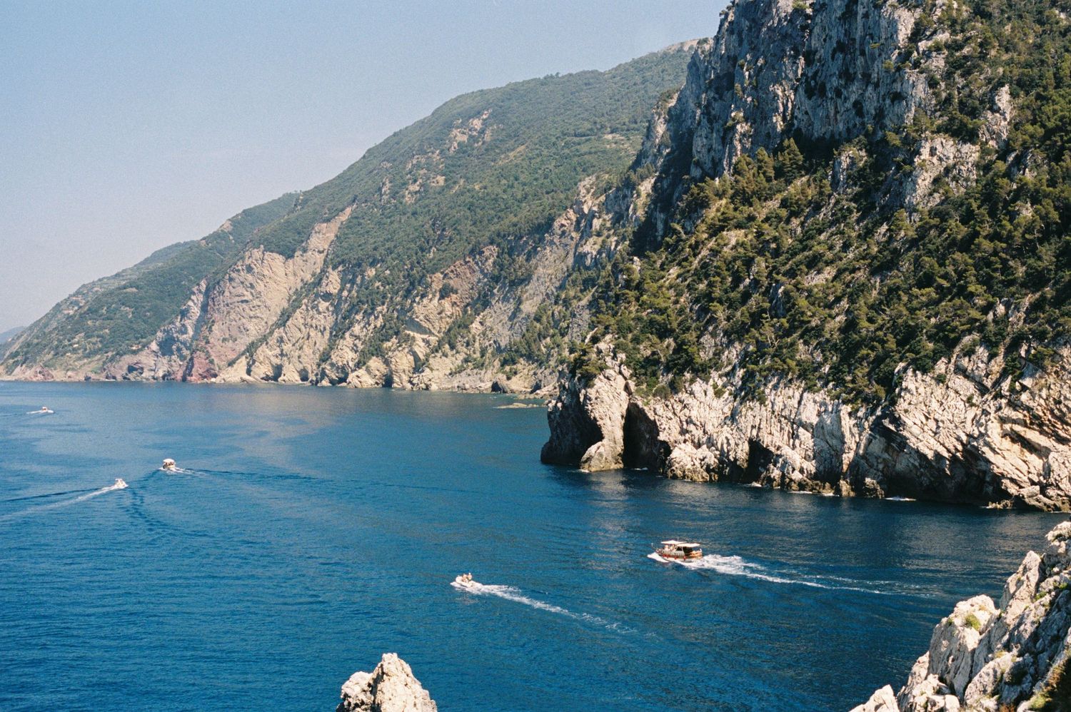 Aerial view of rocky Mediterranean coastline with deep blue waters and two boats sailing near dramatic cliffs and sea caves.