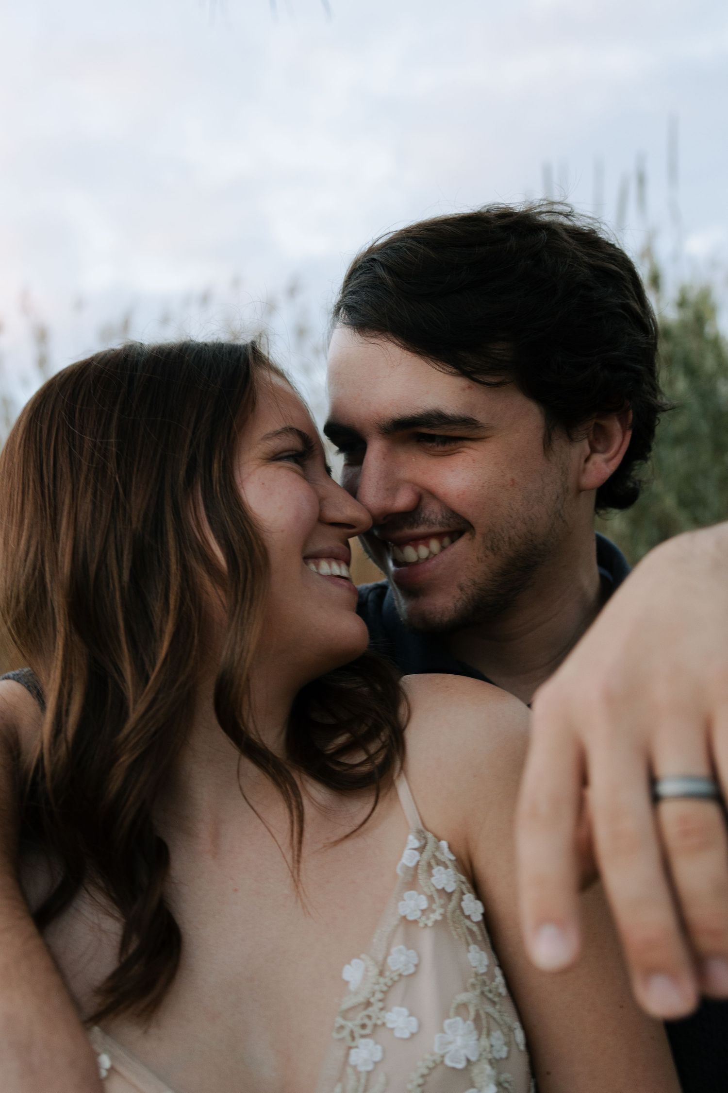 Happy engaged couple smiling and touching noses, man wearing silver wedding band outdoors.