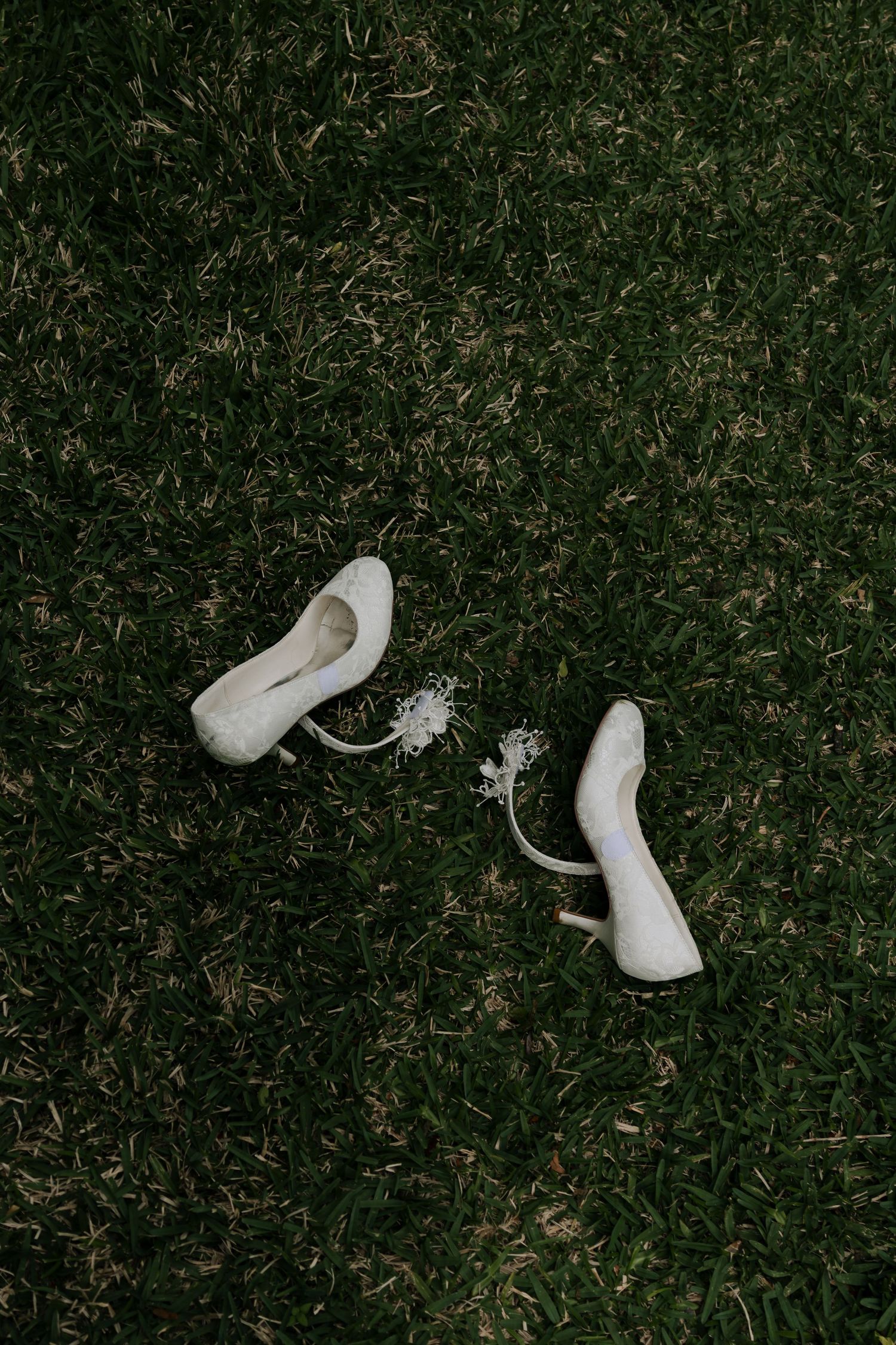 White bridal heels with floral anklets resting on lush green grass at a wedding.