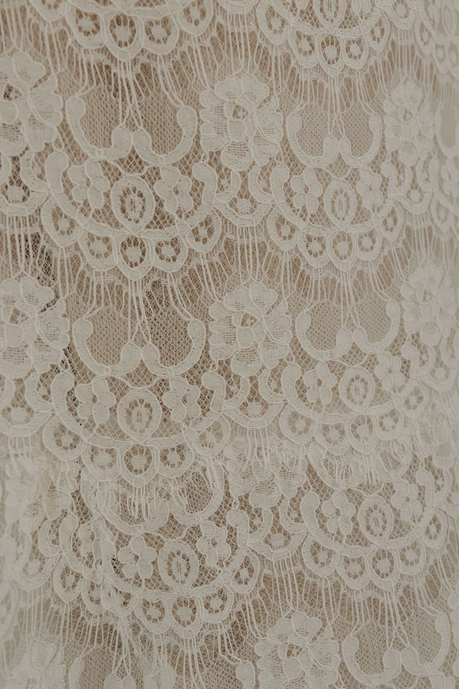 Delicate ivory floral lace fabric with intricate scalloped patterns and circular motifs, perfect for bridal or formal wear.