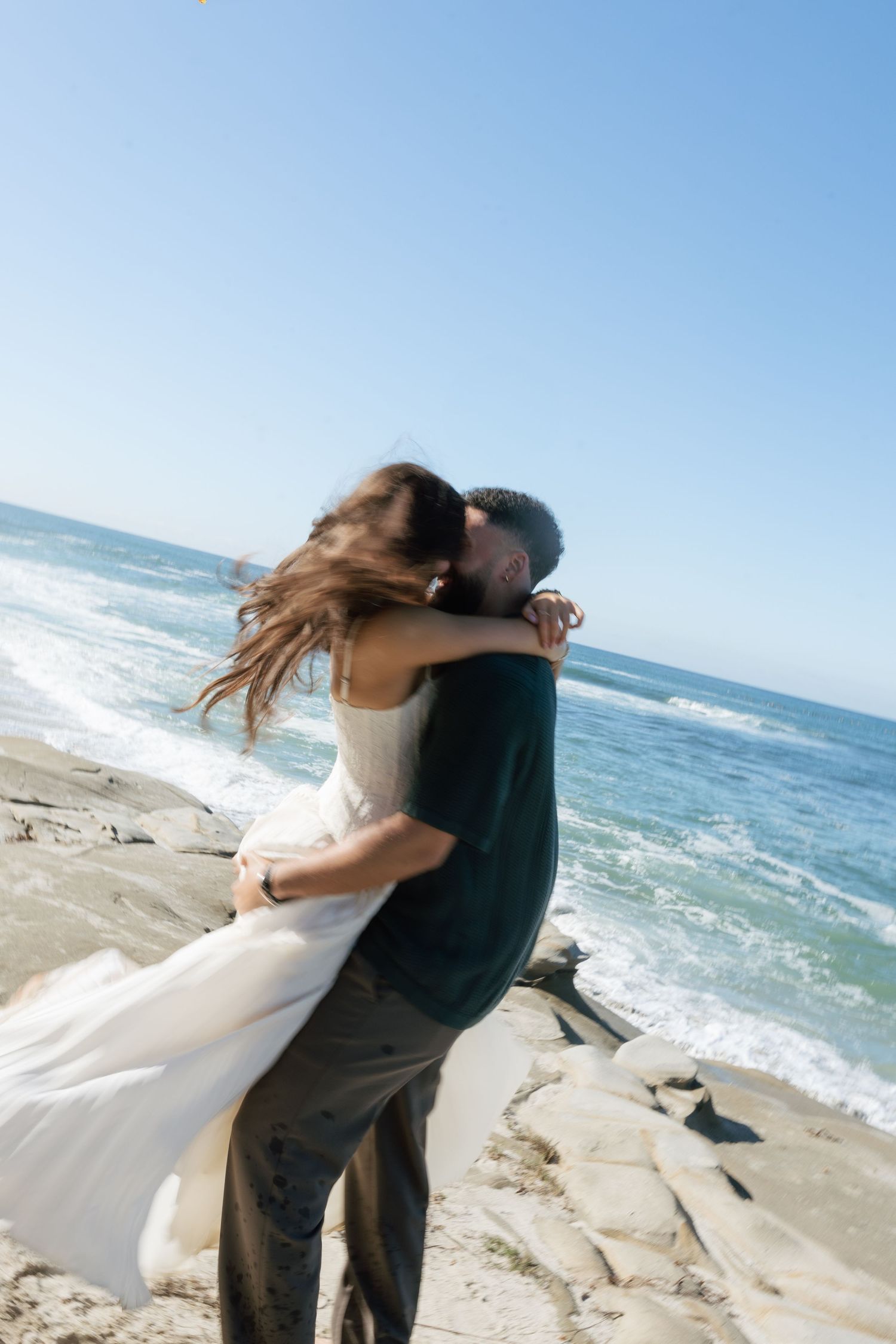 Romantic beach wedding photoshoot with crashing waves and ocean backdrop.