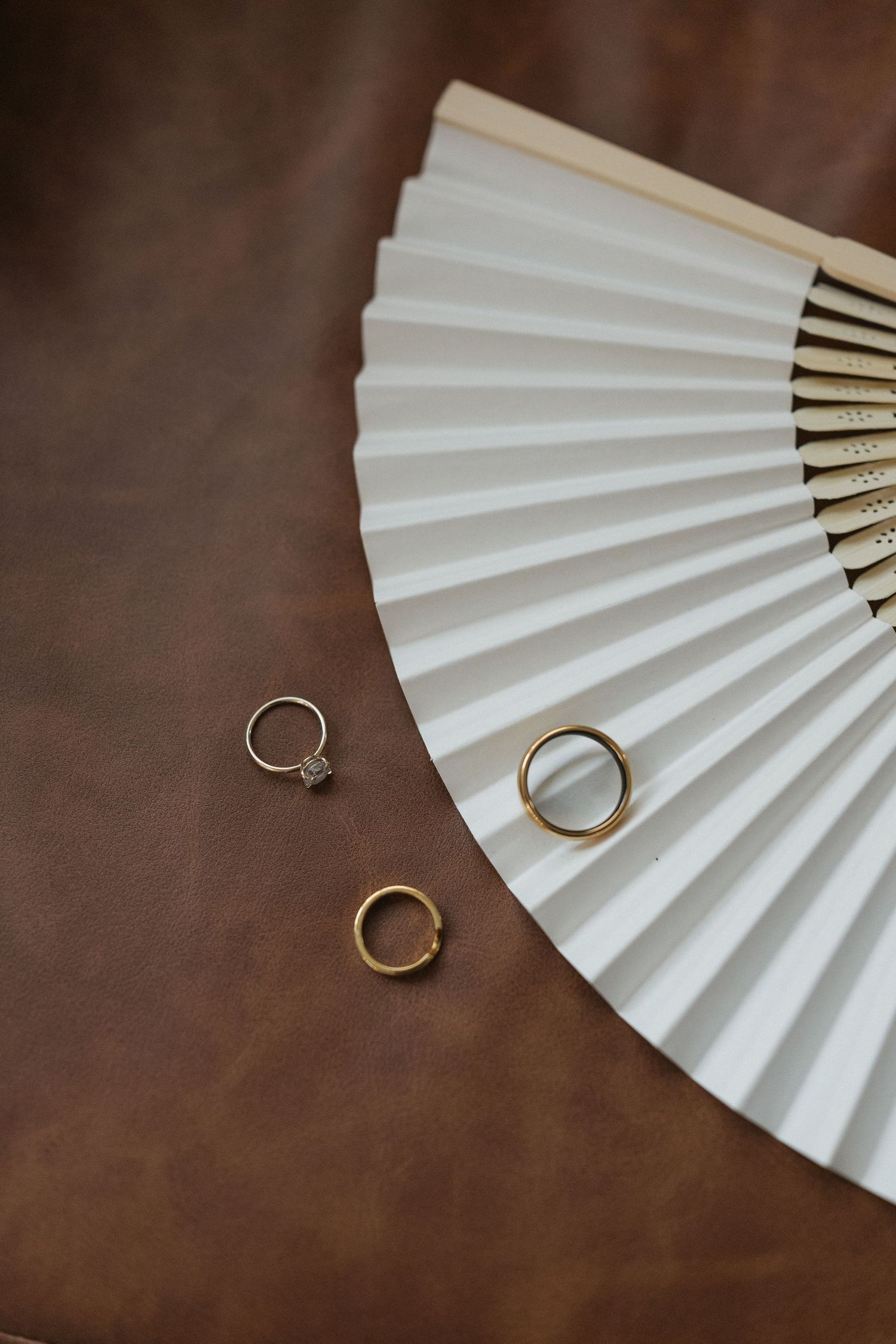 Three gold rings displayed on a white folding fan against brown leather background.