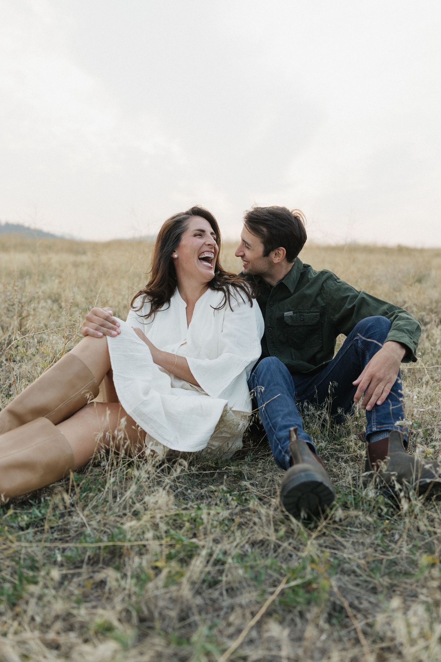 A couple laughing together while lying in a grassy field.