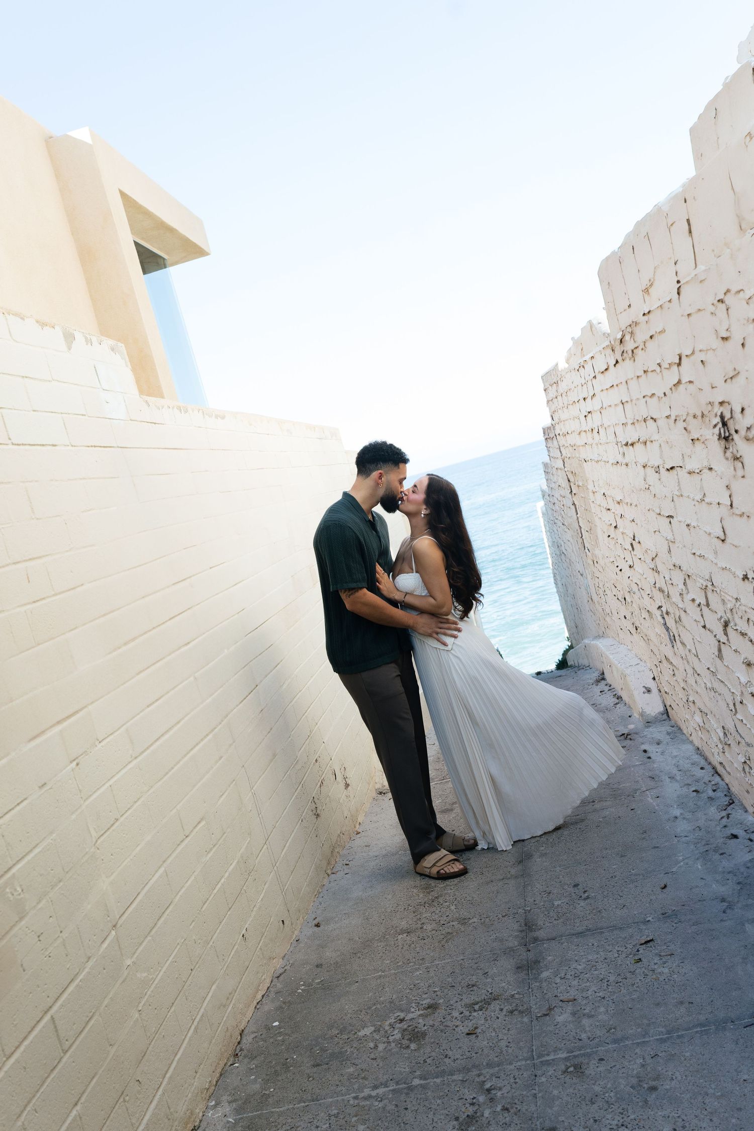 Wedding couple shares intimate moment against geometric white wall architecture.