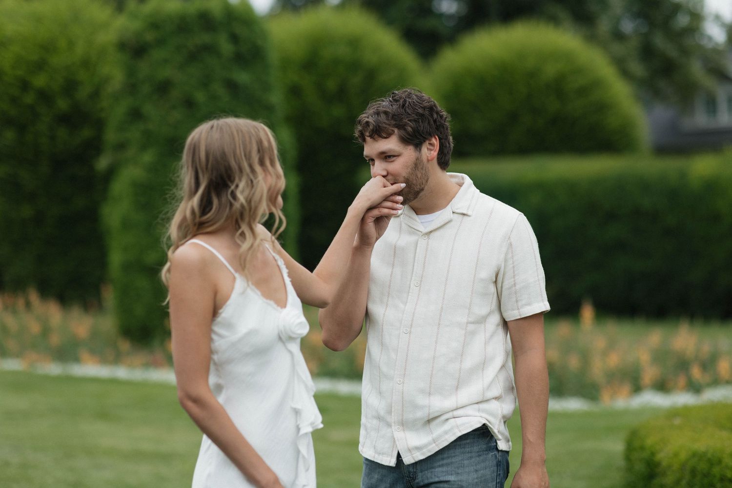 A candid moment between a couple in a garden setting with manicured hedges.