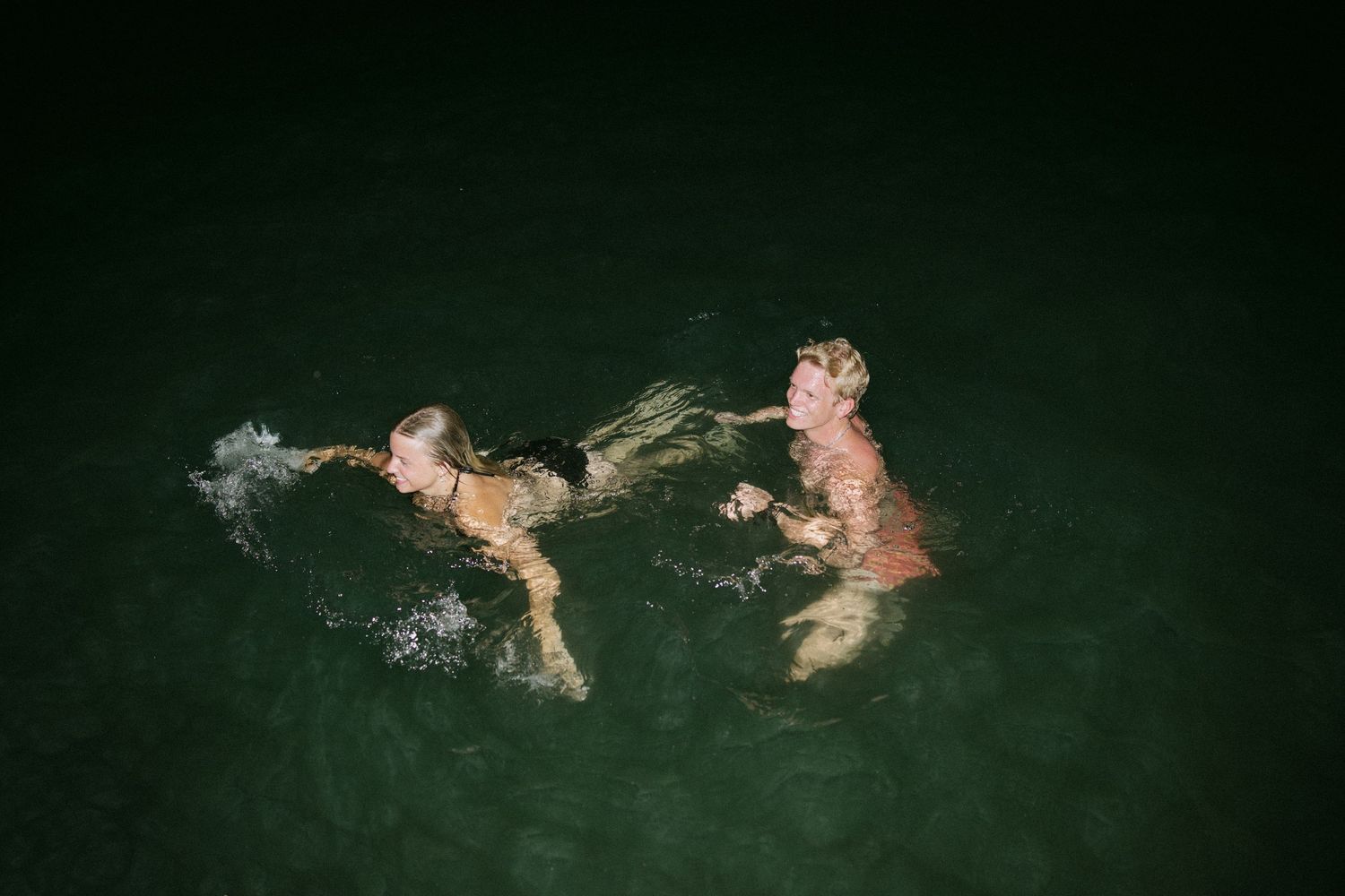 Silhouettes of people swimming in dark water at night.