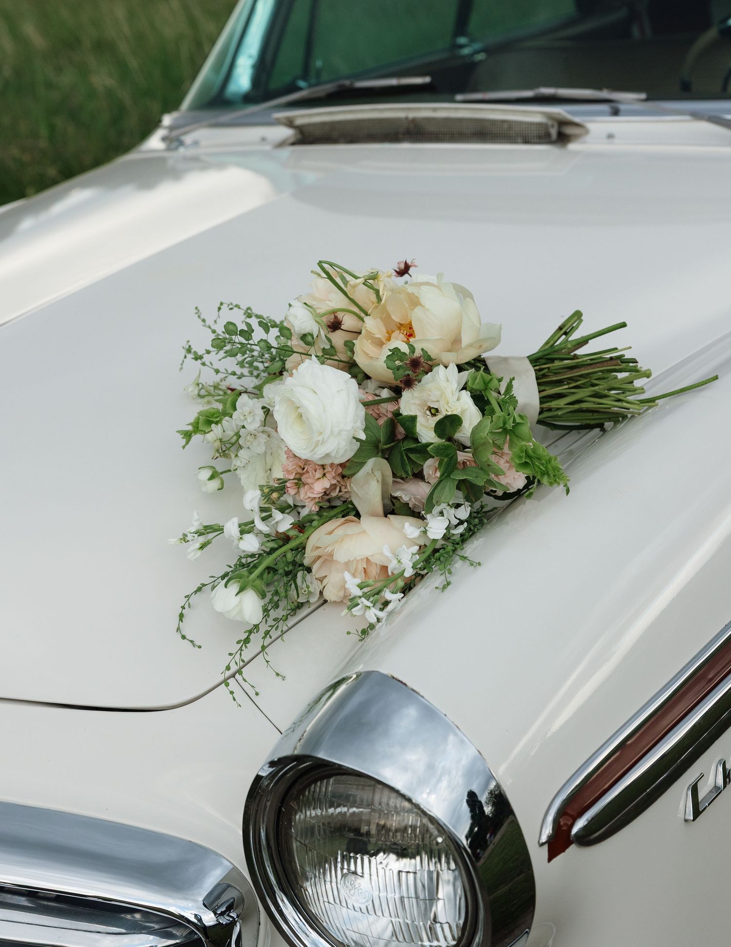 White vintage wedding car hood adorned with an elegant bridal bouquet of white and blush roses with greenery.