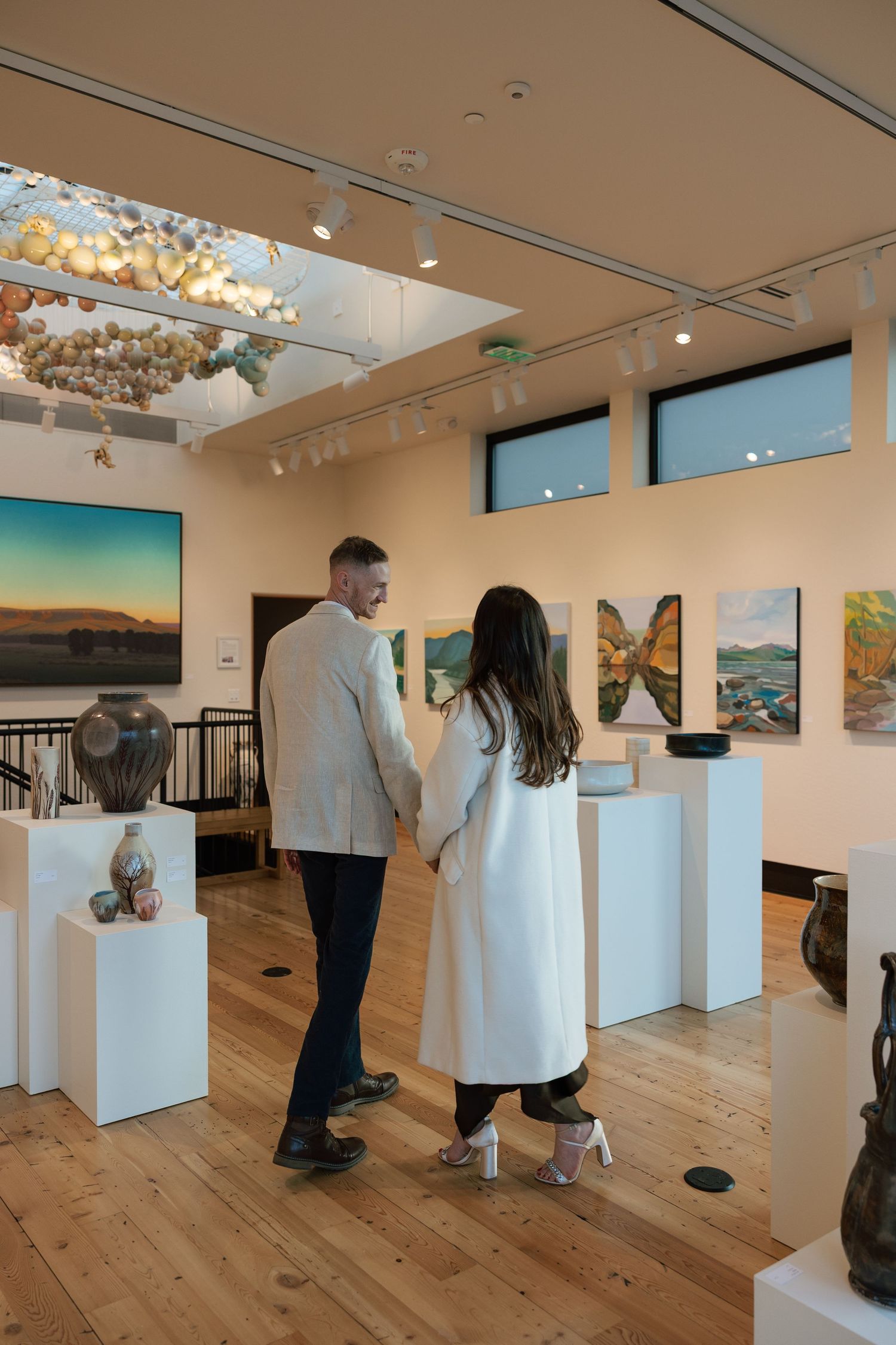 Couple views artwork in modern gallery space with wooden floors and white walls.