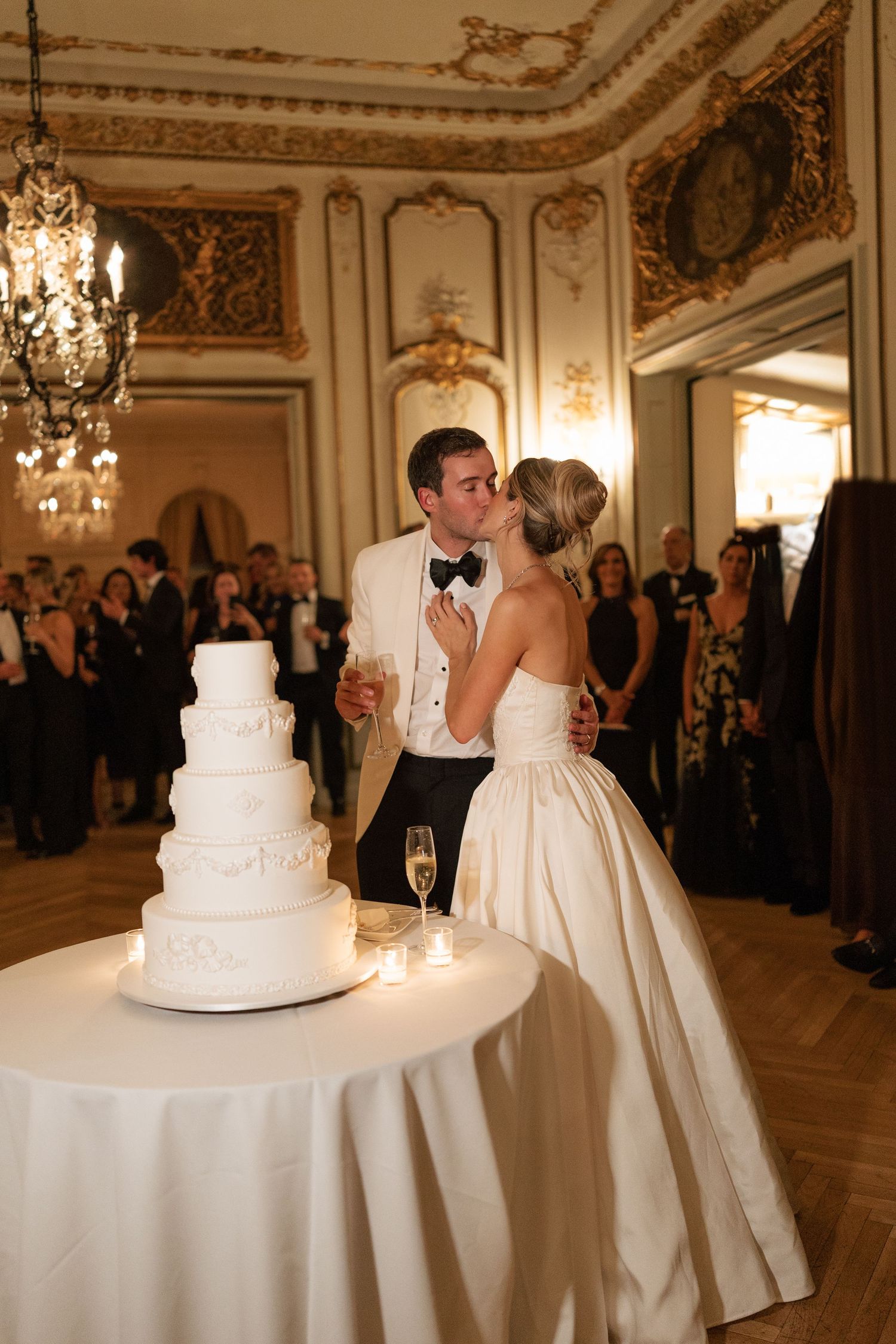 Elegant wedding reception in ornate ballroom with chandelier and tiered white cake.