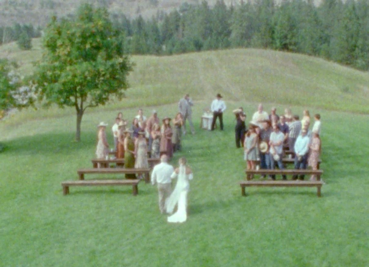 Wedding ceremony setup with wooden benches on a scenic hillside surrounded by trees.