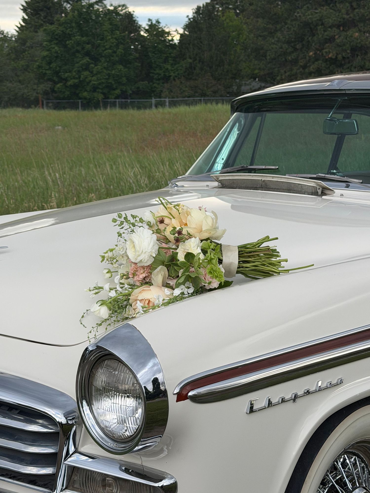 Vintage white Chrysler classic car adorned with elegant bridal floral arrangement of white and pink roses for a wedding.