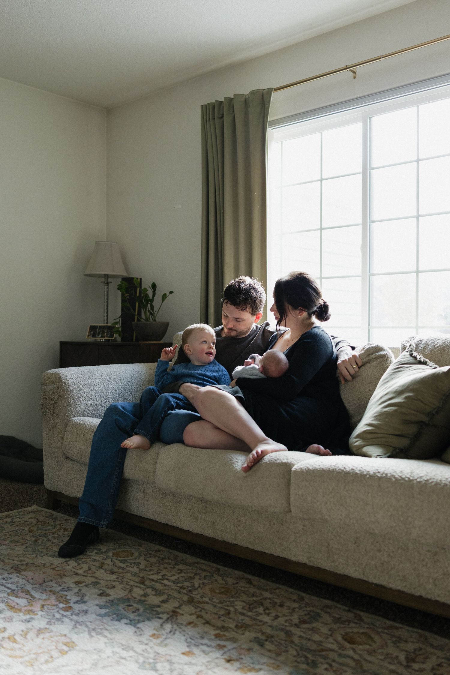 Relaxed family moment on a beige couch in sunlit living room.