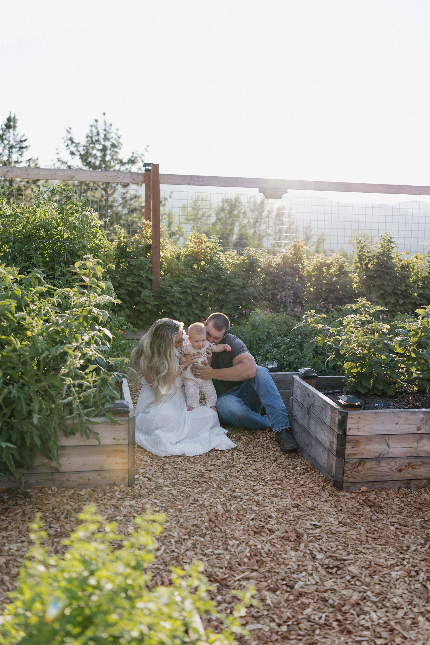 Family sitting together in rustic garden with raised wooden planters at sunset.