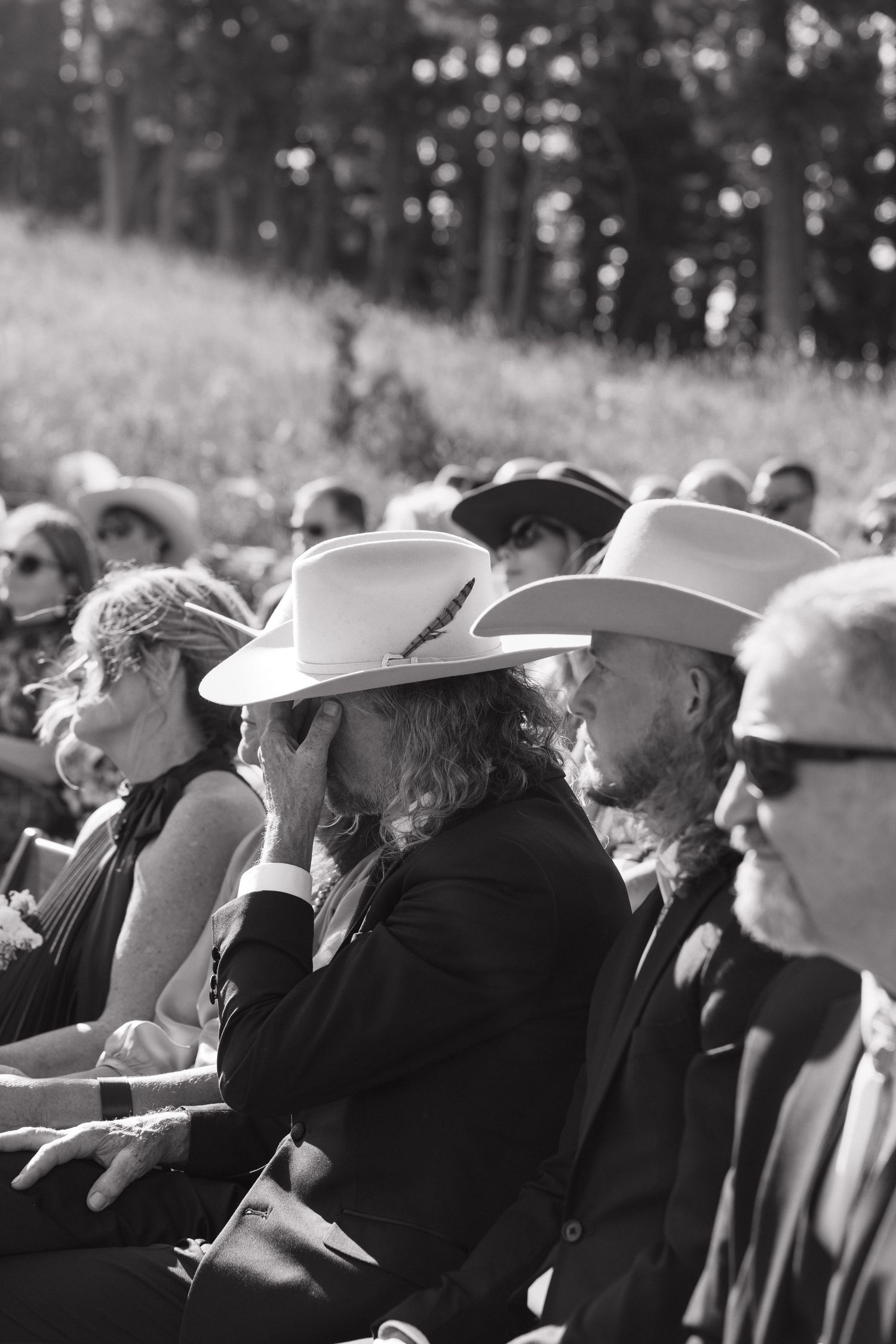 Black and white photo of wedding guests wearing hats watching ceremony.