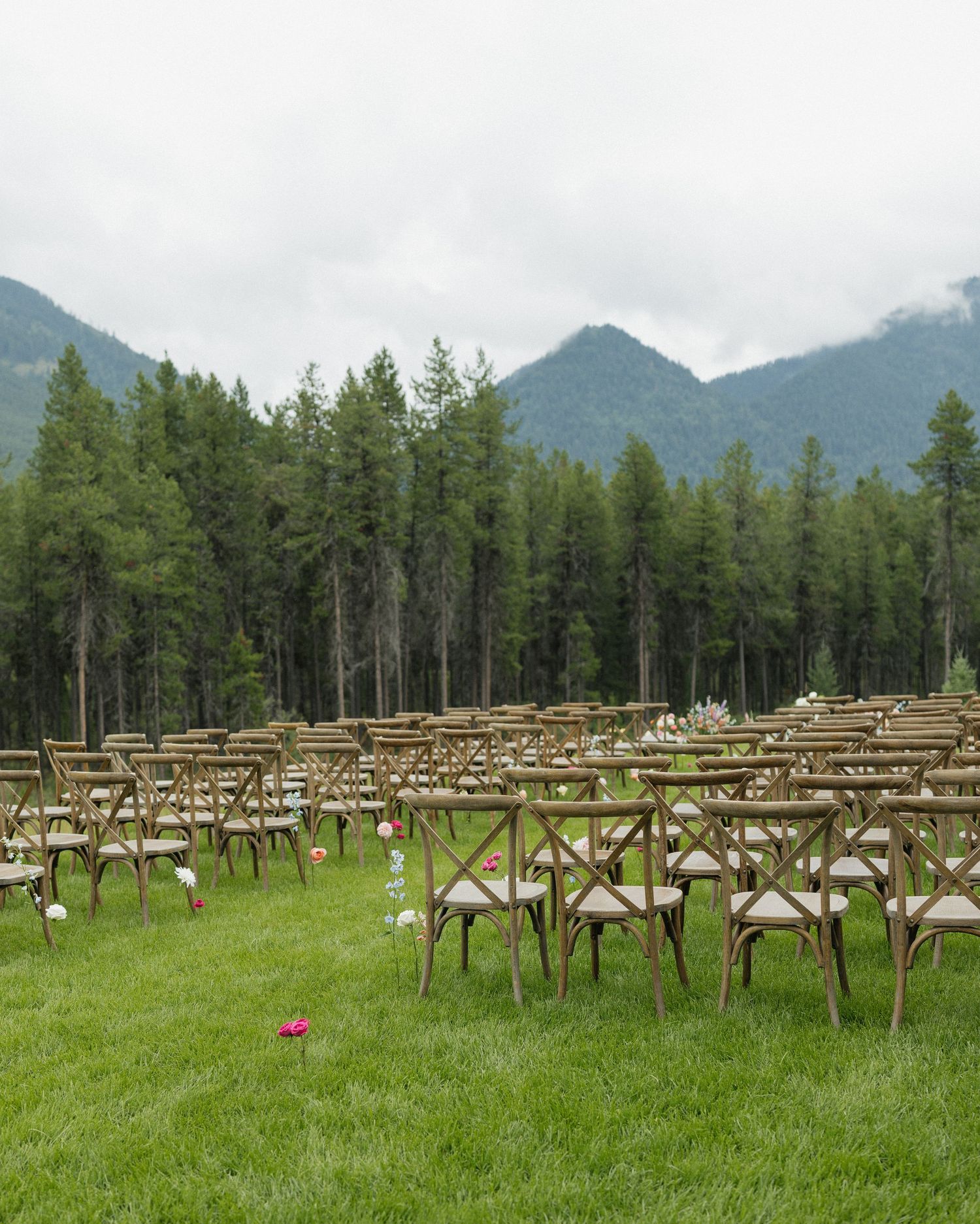 Rustic outdoor wedding ceremony setup with wooden chairs arranged in rows against mountain backdrop.