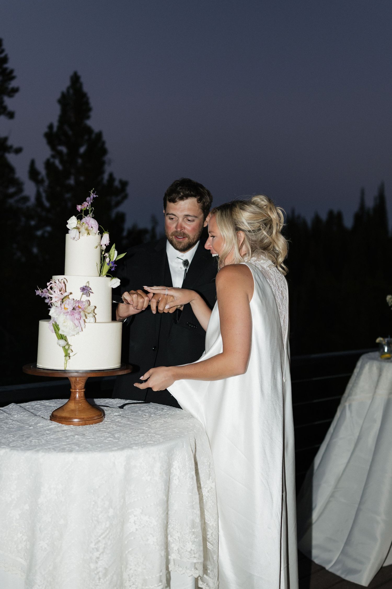 Wedding couple cutting their elegant white tiered cake decorated with fresh flowers.