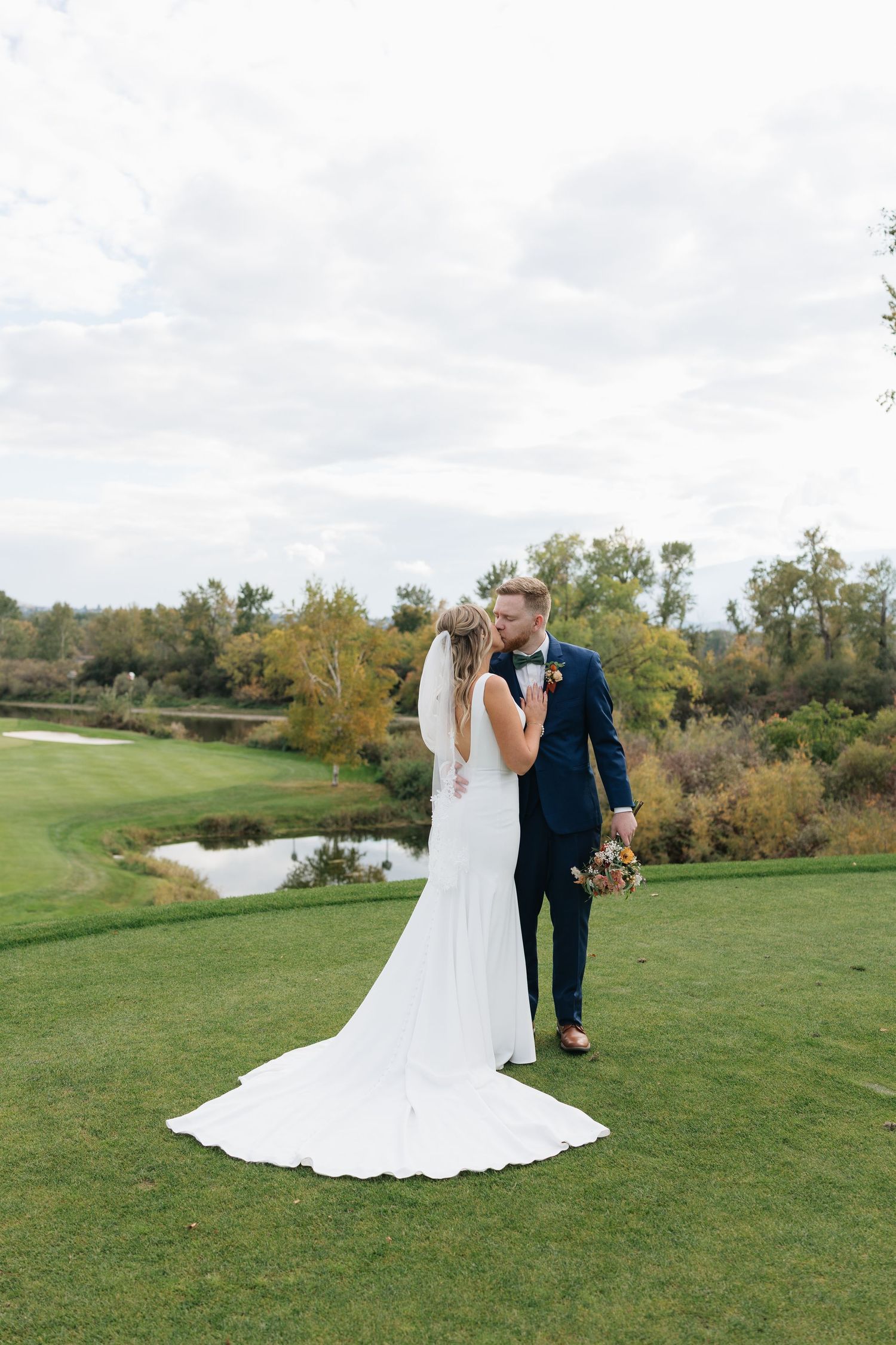 Wedding couple poses in an outdoor setting with green grass and a pond in the background.