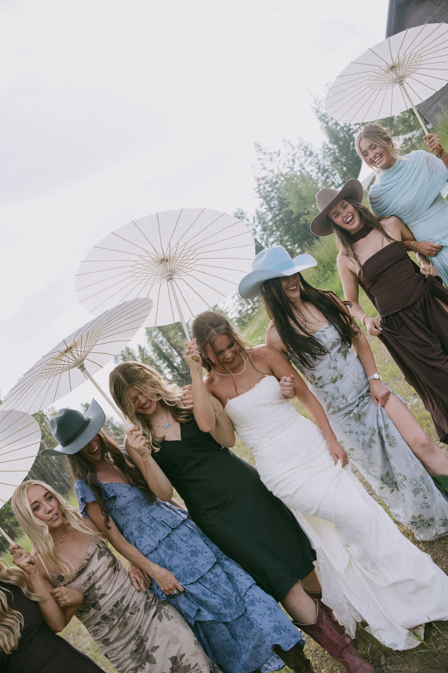 Wedding party holding white parasols outdoors against a scenic mountain backdrop.