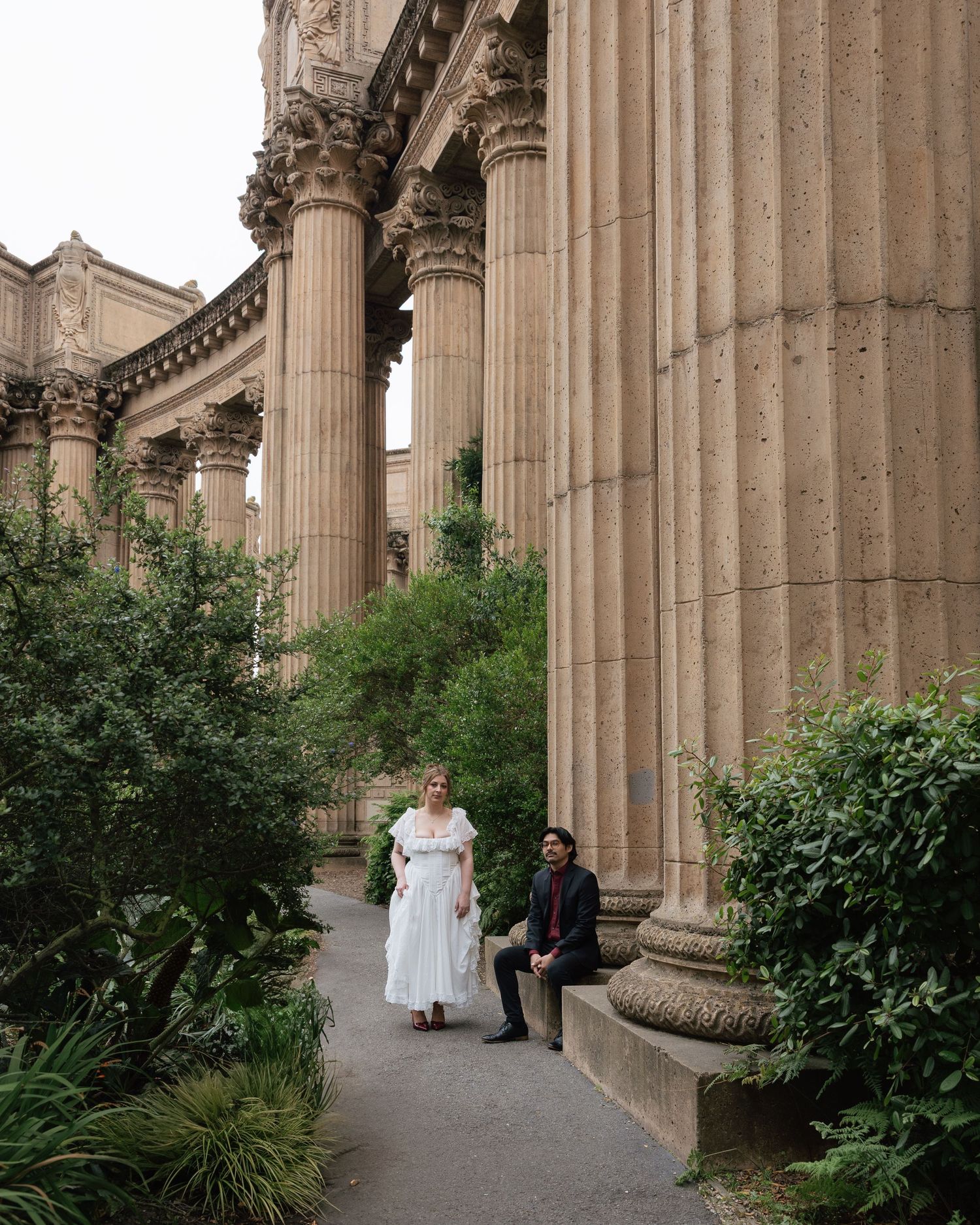 Couple poses among towering Corinthian columns and lush greenery at the Palace of Fine Arts in San Francisco.