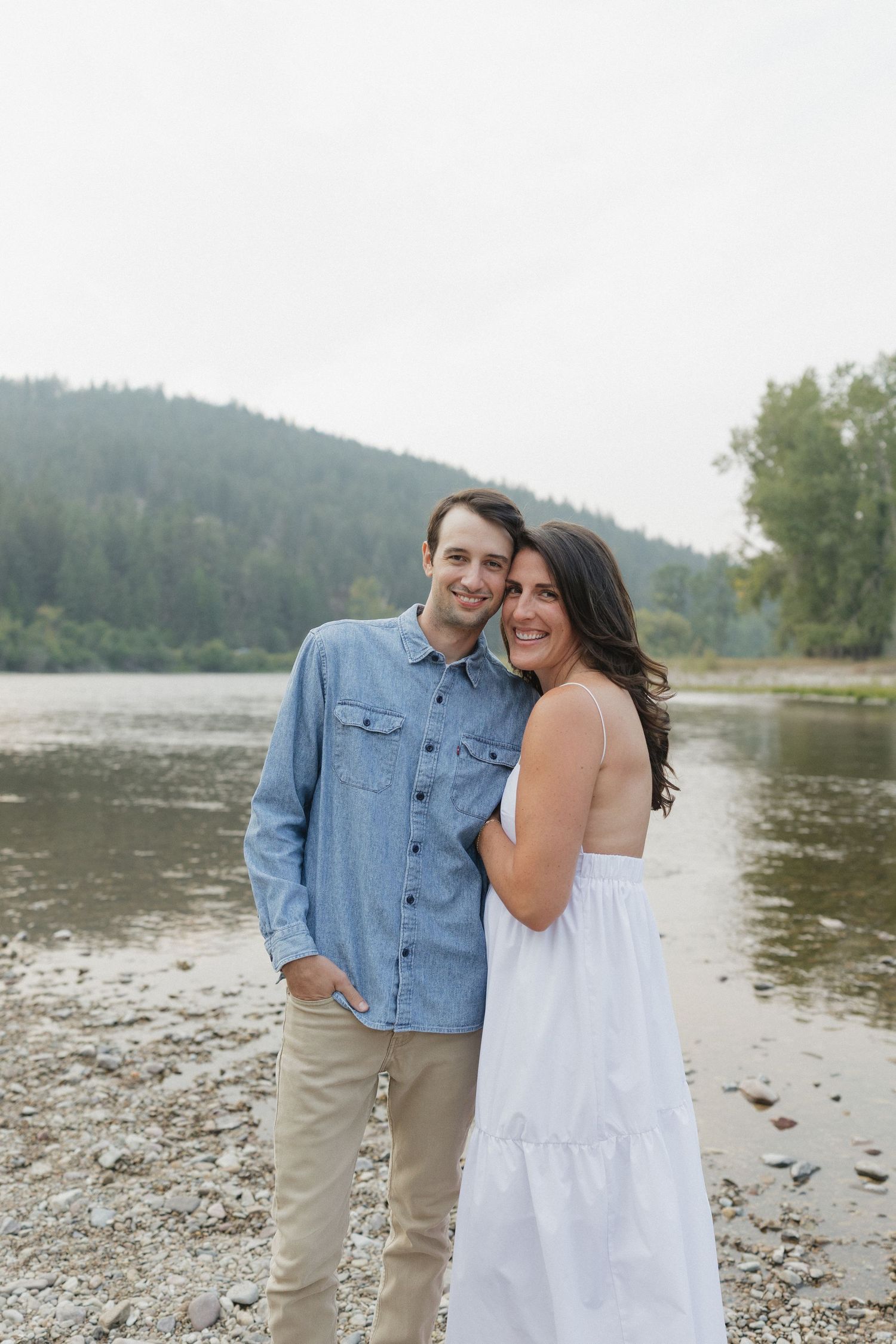 A joyful couple sharing laughter on a rocky lakeshore.
