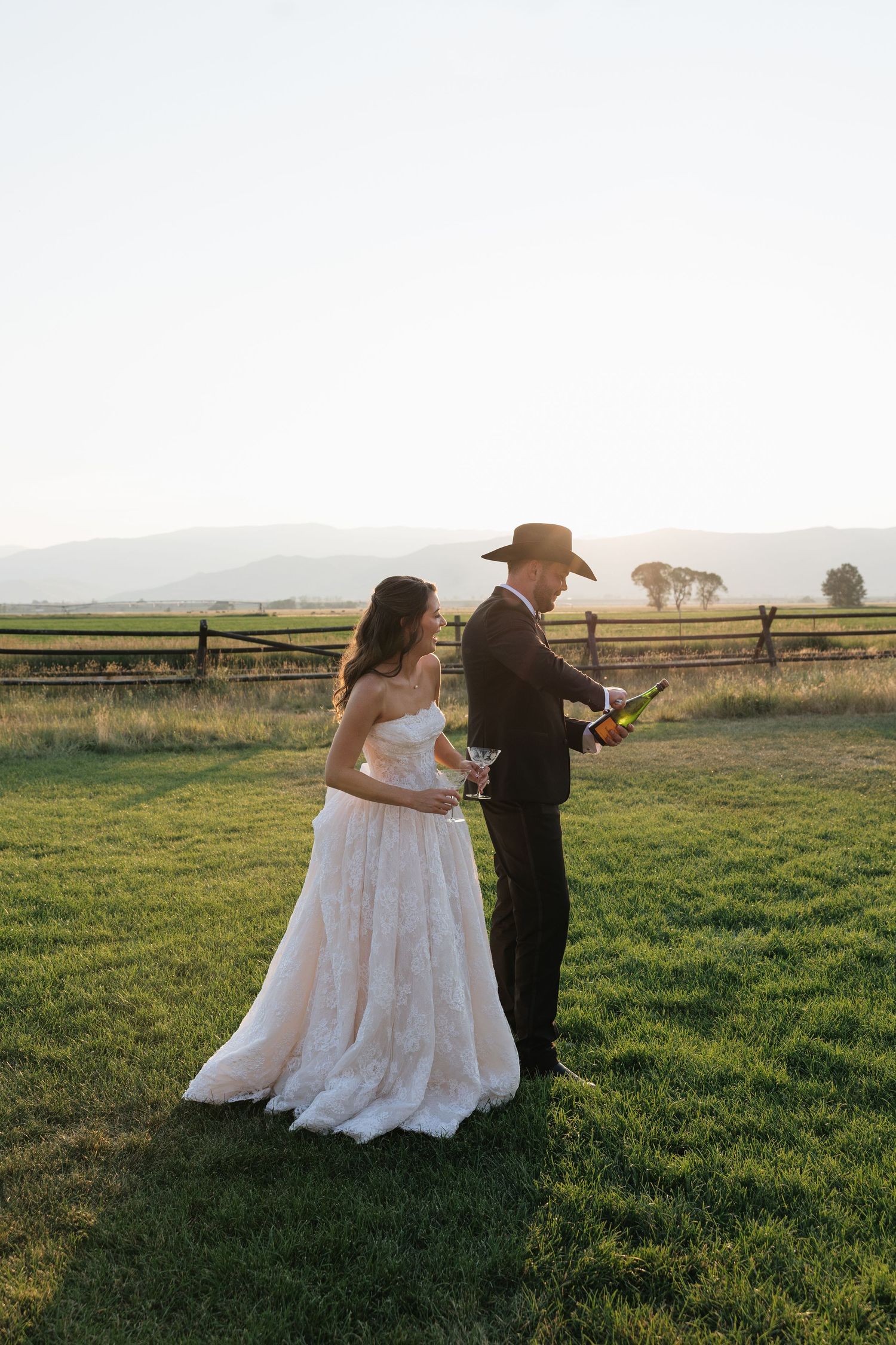 Bride and groom celebrating with champagne at sunset on a green lawn with mountain views at an outdoor wedding.