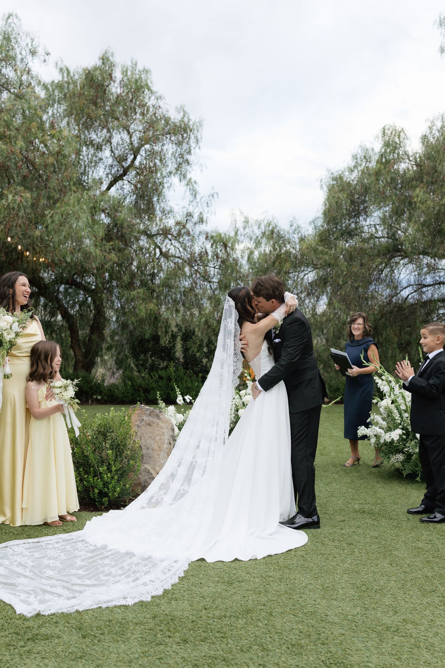 Garden wedding ceremony under willow trees with flowing white dress and veil.
