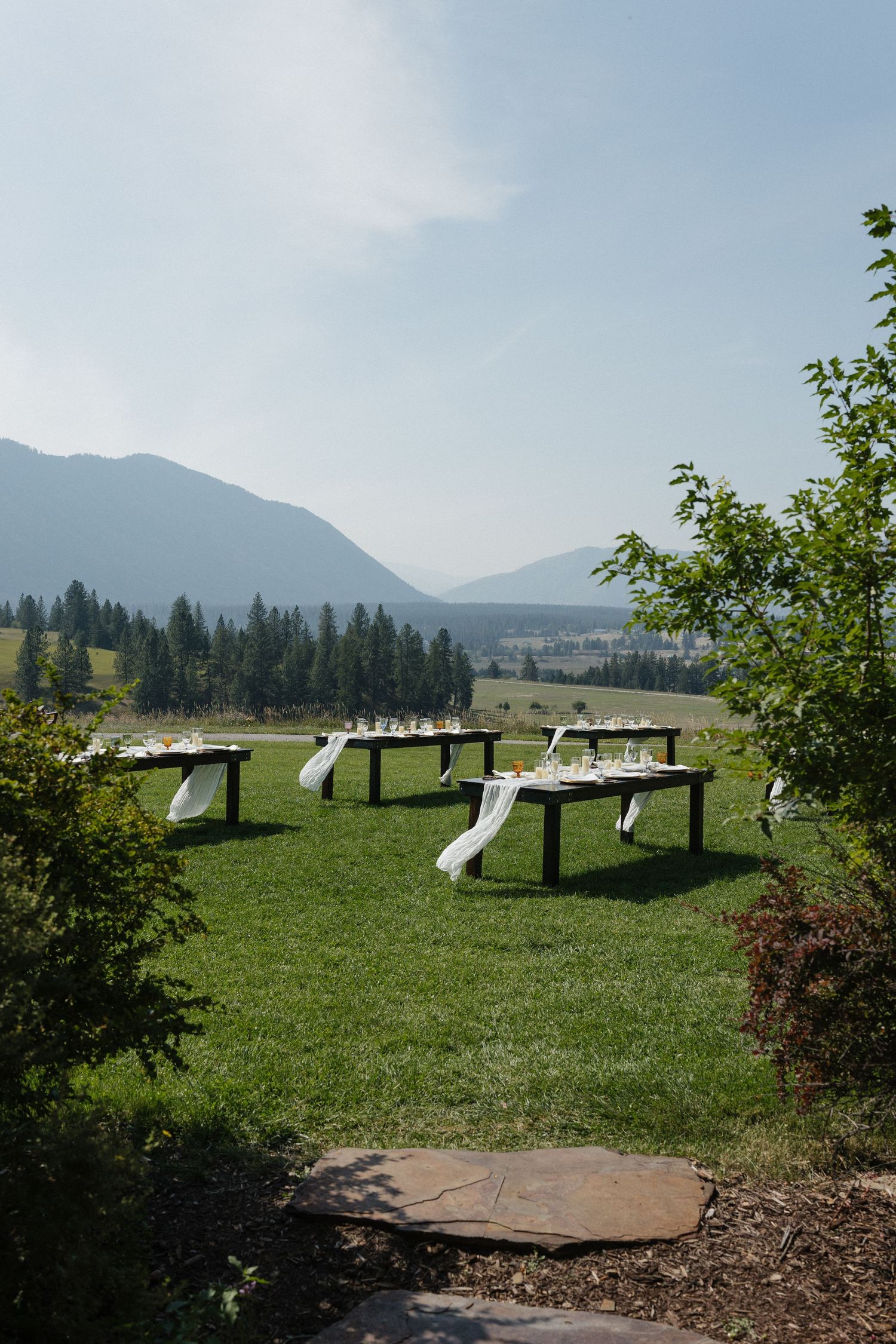 Outdoor mountain venue with picnic tables arranged on a grassy hillside surrounded by evergreen trees.