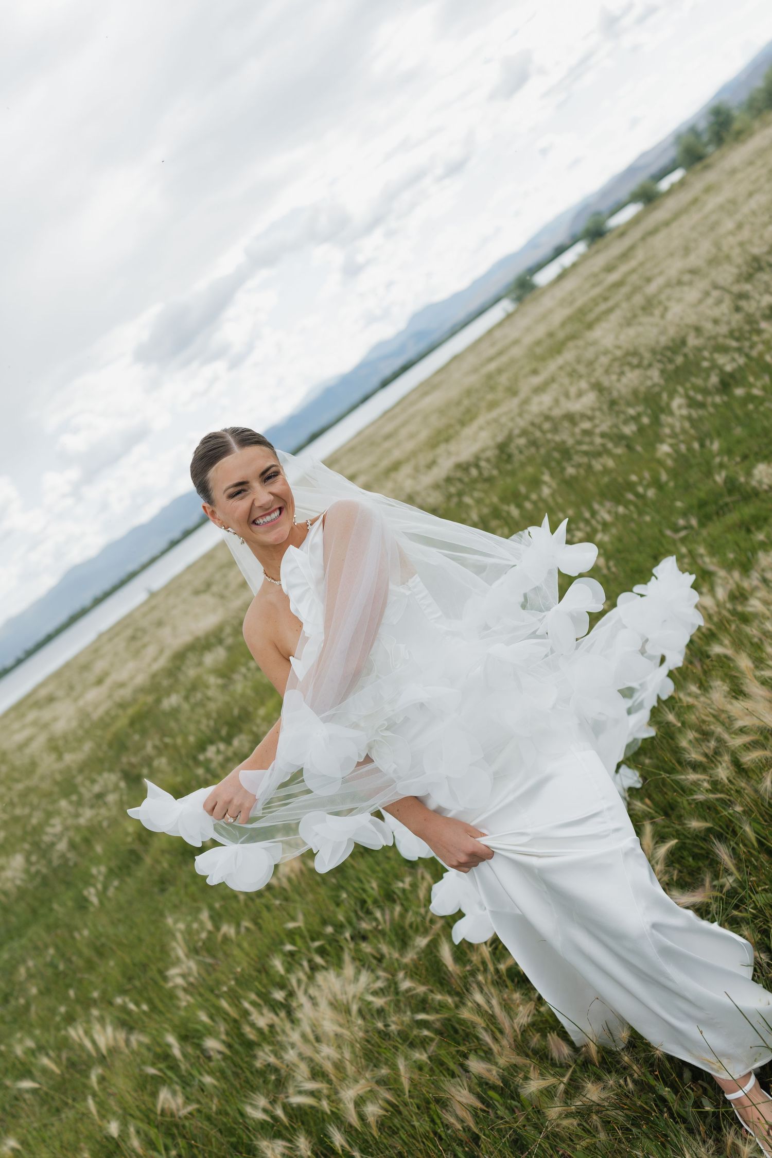 Bride in flowing white dress twirls joyfully on a hillside overlooking a scenic landscape.