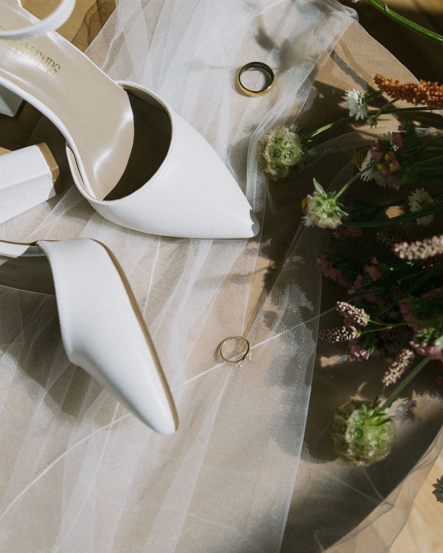 Wedding accessories including white heels and rings artfully arranged with delicate floral elements.
