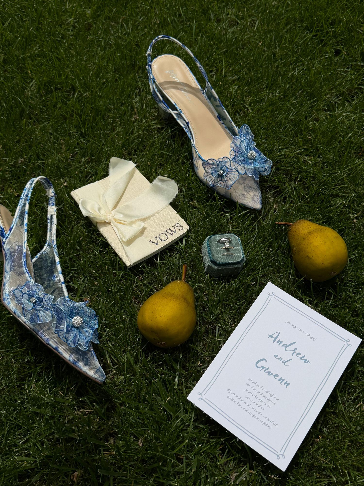Blue floral wedding heels on grass with invitation, ring box, pears, and Vows booklet for Andrew and Gwen.
