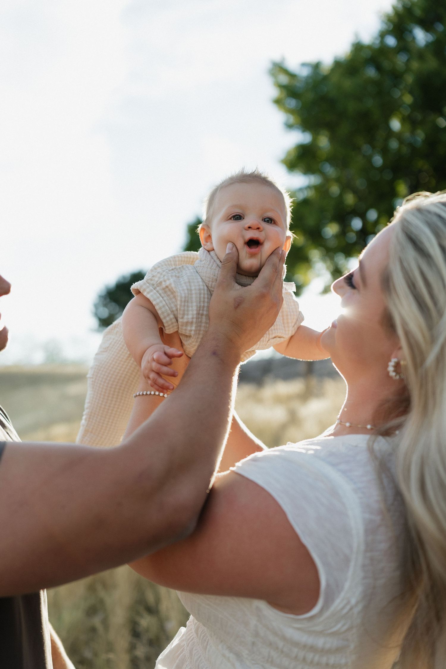 Candid moment of joy and laughter with baby held up in outdoor setting.