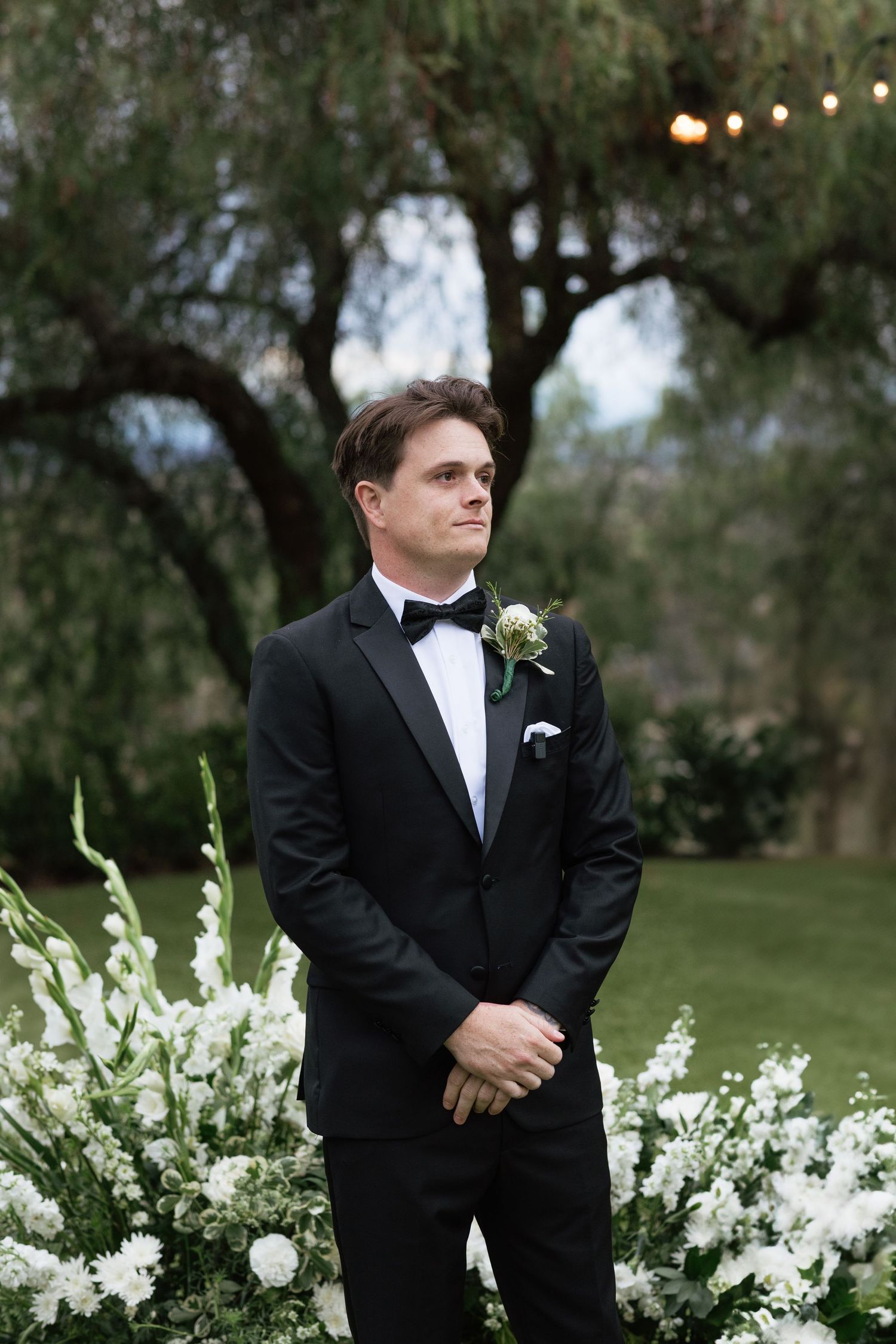 Classic formal attire against white floral garden backdrop.